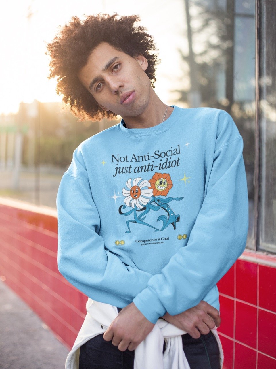 Model wearing a light blue sweatshirt with playful cartoon flower design and "Not Anti-Social just anti-idiot" text.