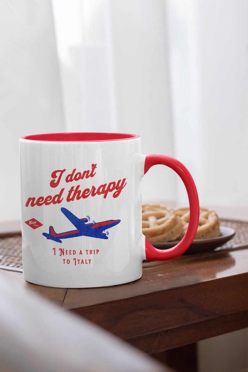 White mug with red interior, featuring text "I don't need therapy I need a trip to Italy", is resting on a wooden board.