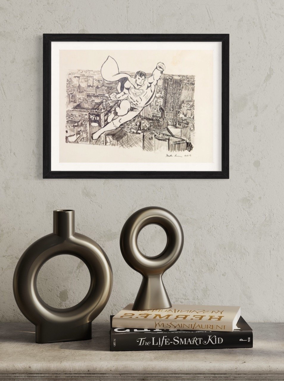"
A framed artwork by Kristin Simmons depicts a superhero flying over a detailed cityscape, displayed on a textured wall. Below it are two ornamental vases and a stack of books."