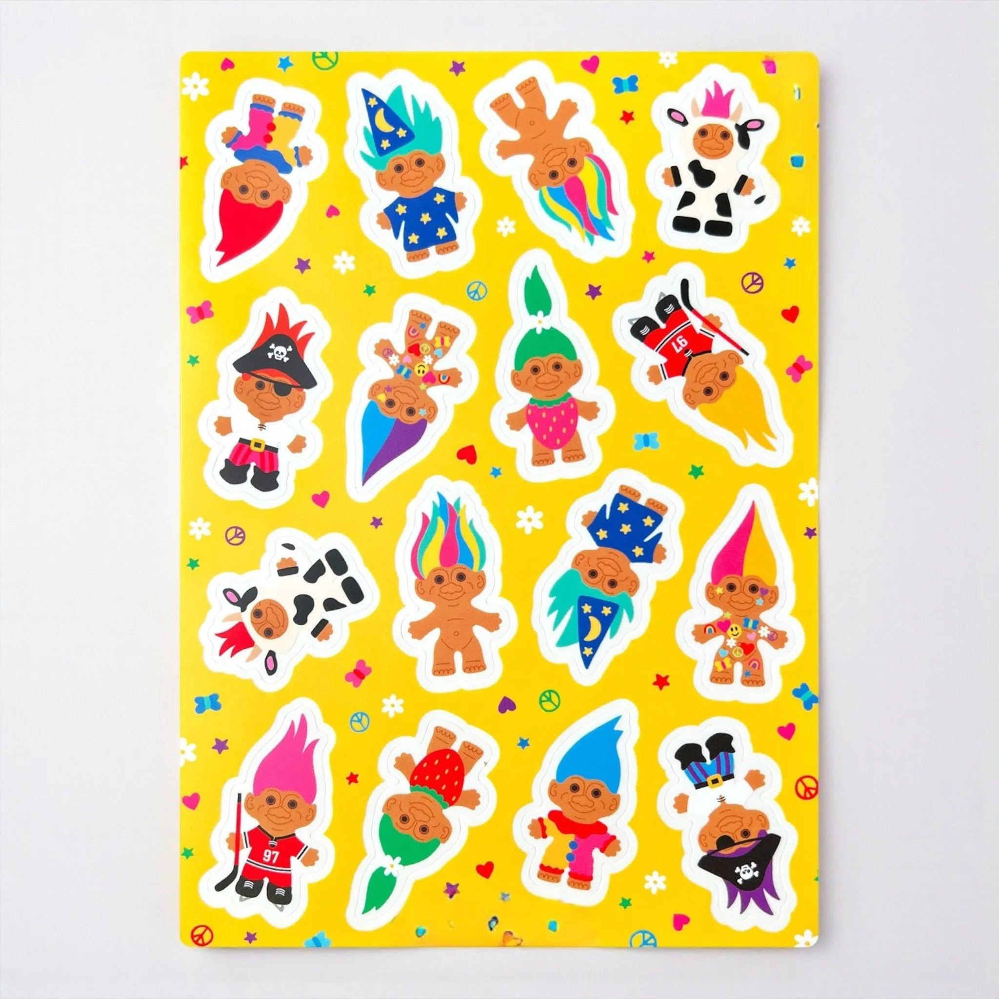 Sticker sheet of colorful troll dolls in costumes with rainbow hair on a yellow background.