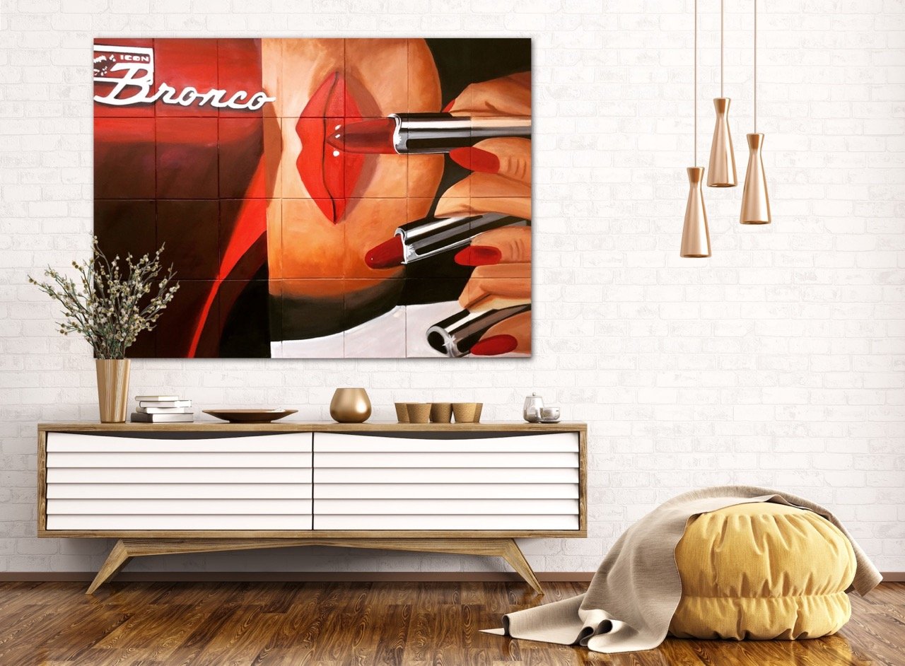 Pop-art inspired painting of a women with bright red nails applying red lipstick tubes in paralel l to a painting of a red bronco hung above a white console.