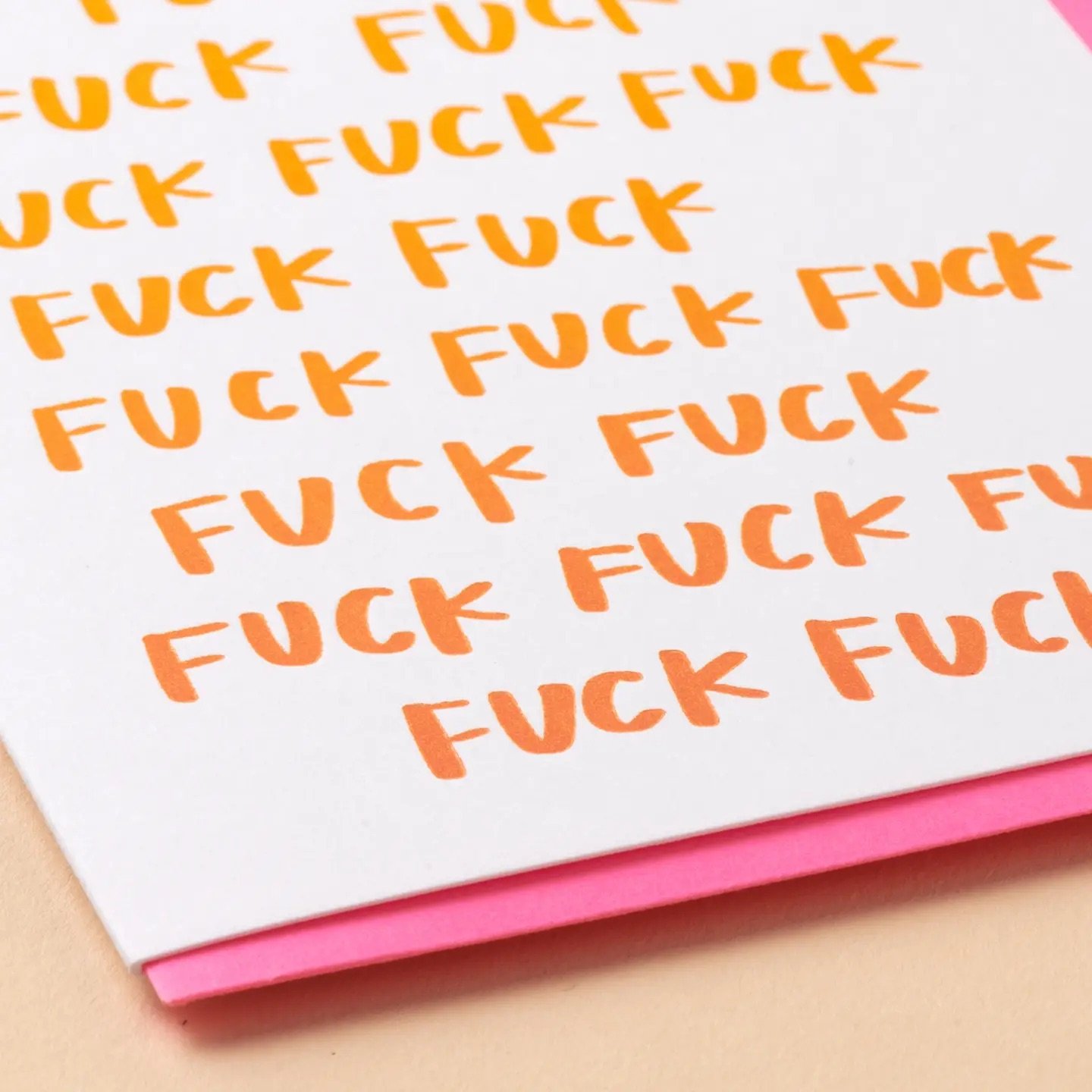 Close-up detail of a funny profanity greeting card with repeated orange “fuck” lettering and a bright pink envelope.