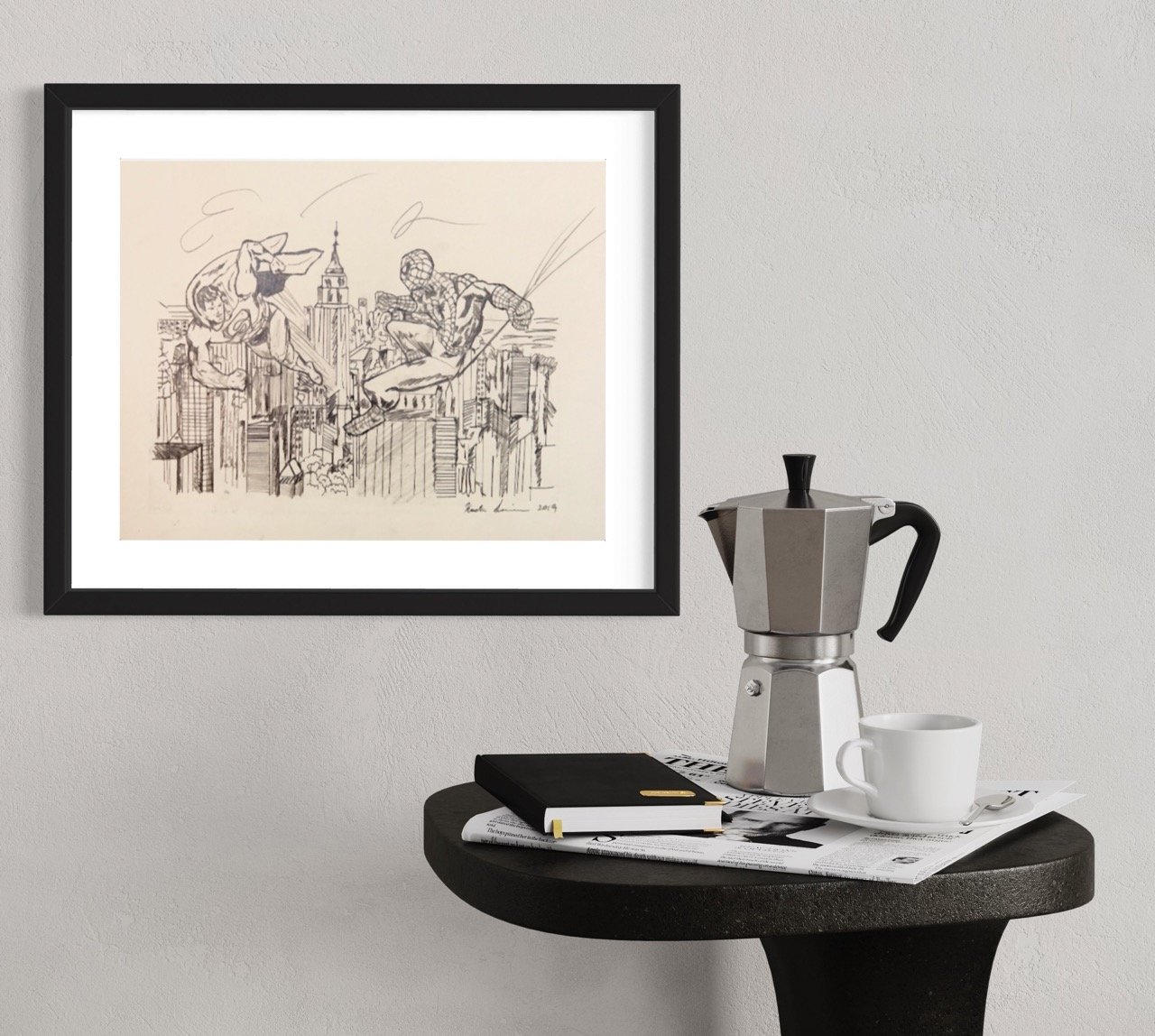 A framed sketch of a bustling cityscape with two superhero figures in action above the skyline, mounted on a light-colored wall. In the foreground, there's a small round table with a metallic coffee maker.
