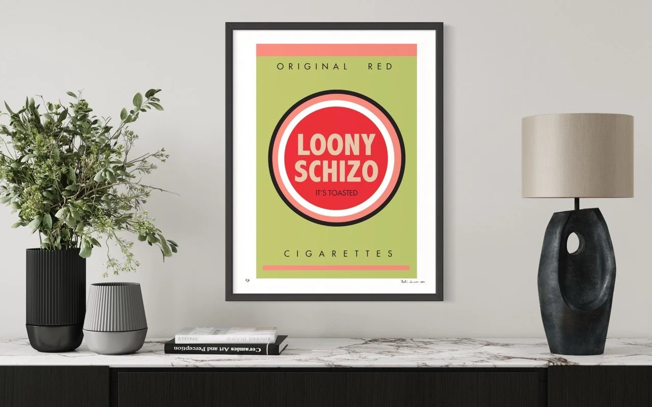 Framed retro-style screenprint on a modern living room wall. The vintage cigarette package design features a green background with a red and white circular logo reading "LOONY SCHIZO" and the tagline "IT'S TOASTED." 