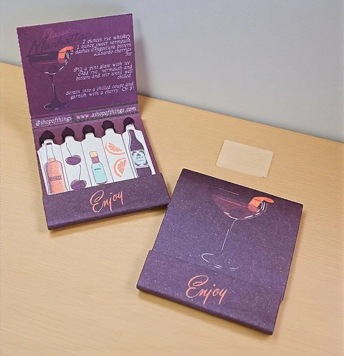 Manhattan cocktail-themed matchbook with whiskey illustrations and vintage burgundy design.