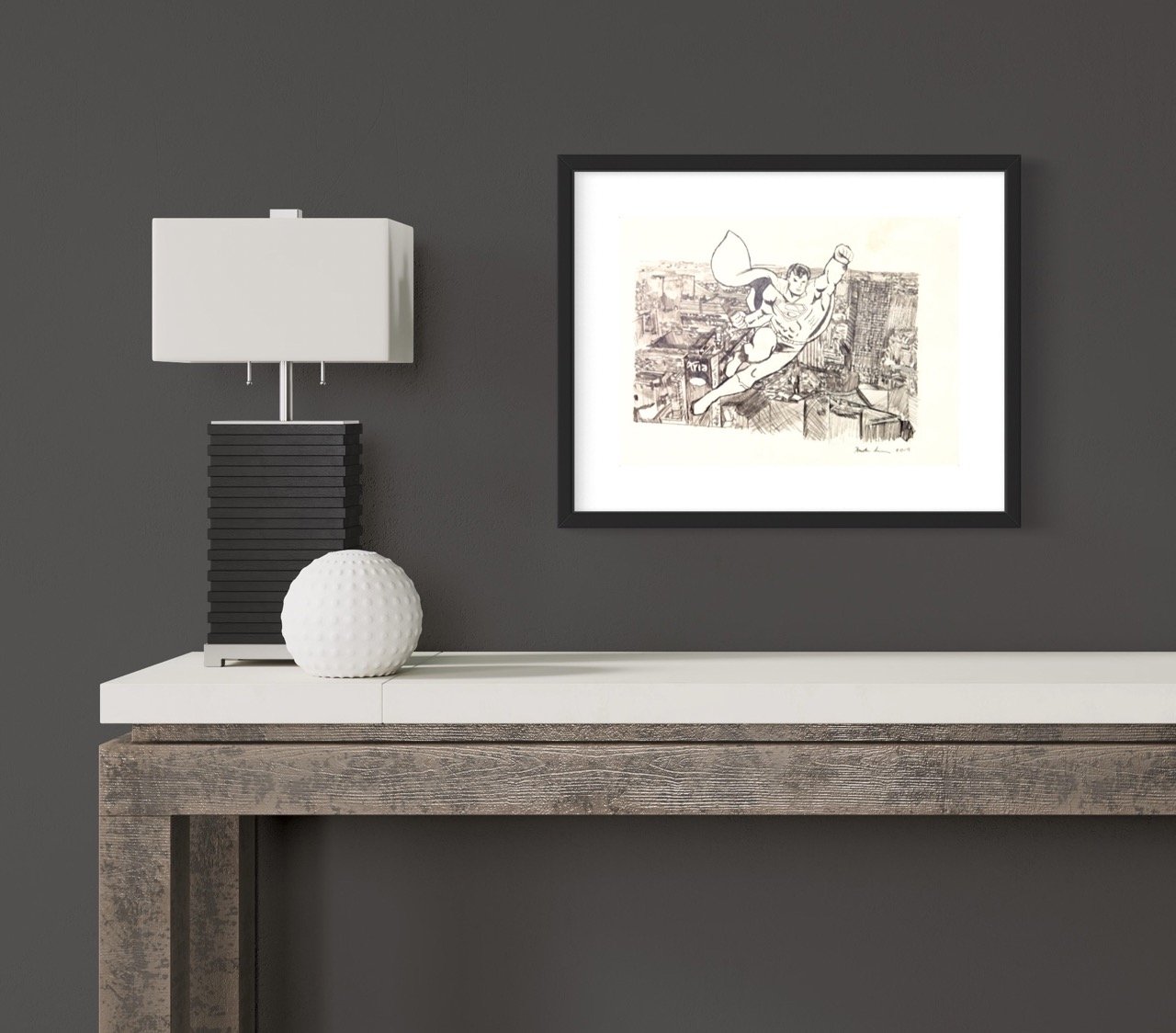 Framed artwork of a superman flying over a cityscape, in monochrome sketch style, displayed on a dark wall beside a modern lamp and textured sphere.