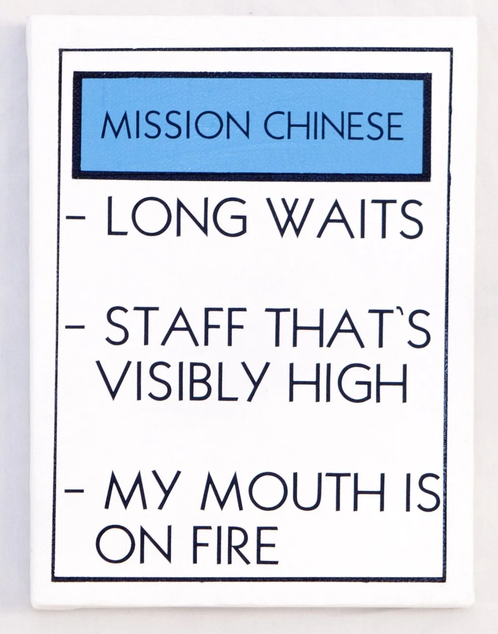 Humorous sign with a blue header labeled "MISSION CHINESE," followed by a bulleted list: "LONG WAITS," "STAFF THAT'S VISIBLY HIGH," and "MY MOUTH IS ON FIRE." The text is in black on a white background, bordered with a black frame.
