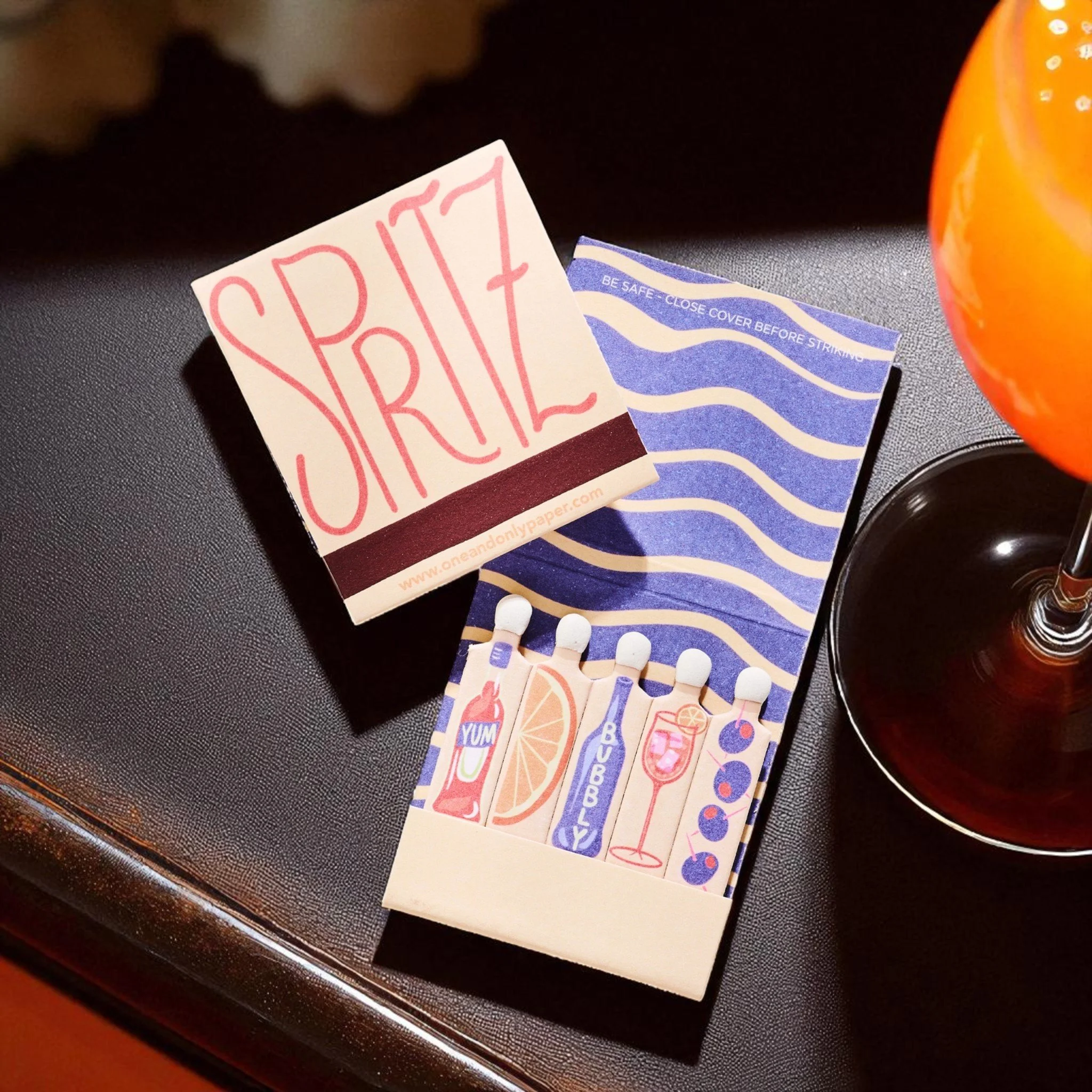 Aperol Spritz matchbook with illustrated bottles, bubbly, citrus, and cocktail glass design.