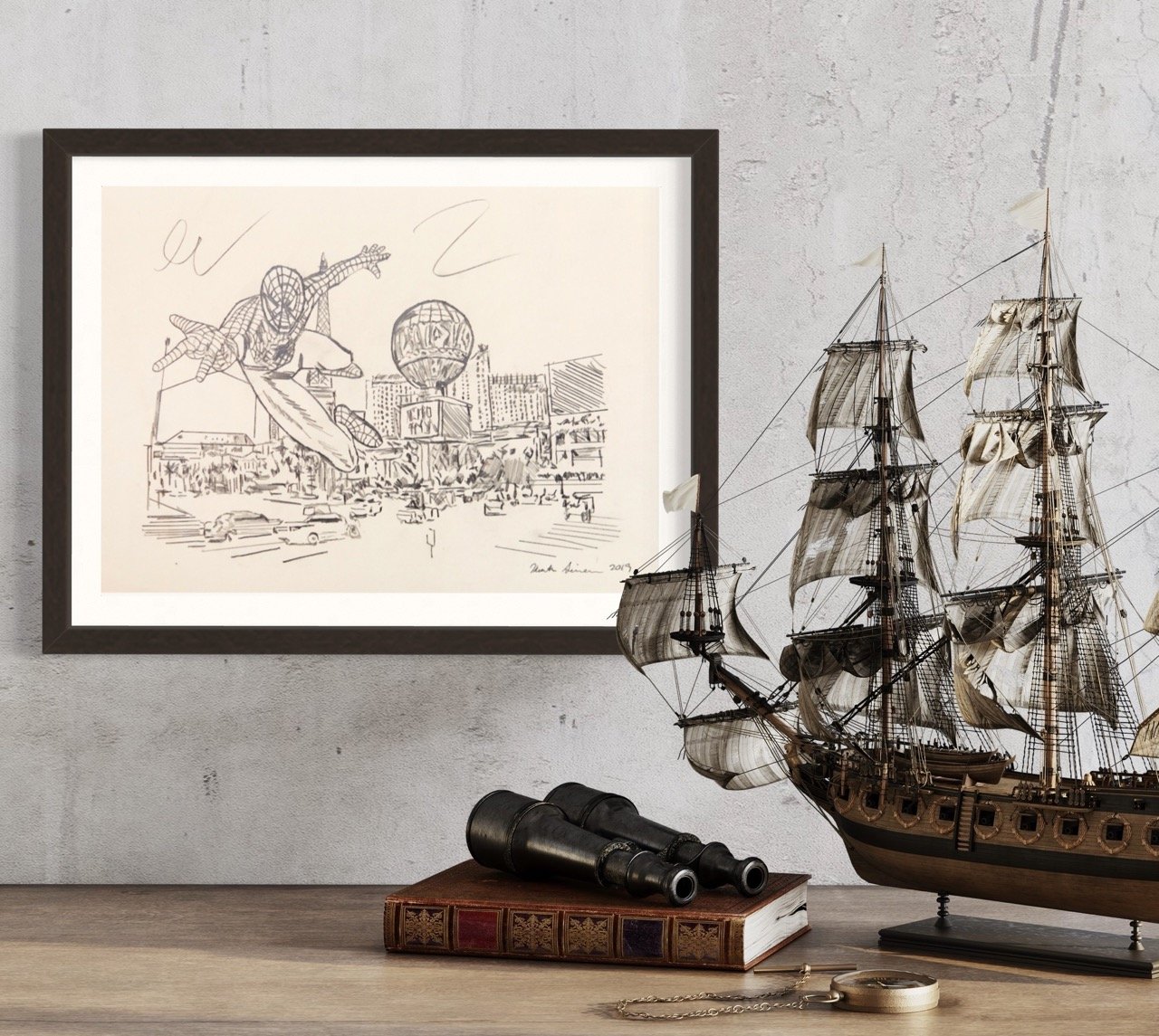 Framed pencil drawing of spiderman flying over las cegas, with expressive movement lines, displayed next to a model ship and vintage books on a wooden table.