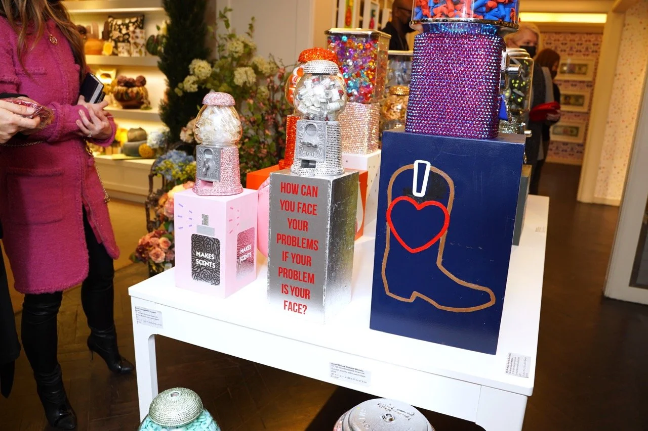 Glittering gumball machine sculptures by Kristin Simmons with text 'HOW CAN YOU FACE YOUR PROBLEMS IF YOUR PROBLEM IS YOUR FACE?' on display.