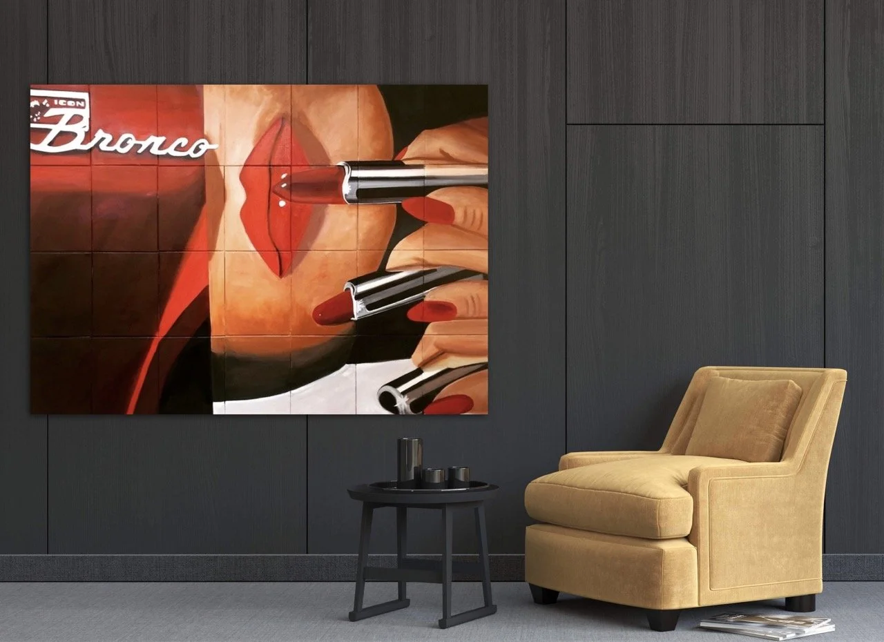 Painting of a red bronco with the logo scripted in juxtaosed on the same canvas with a painting of a woman with red nails applying red lipsticks hung against a black wall.