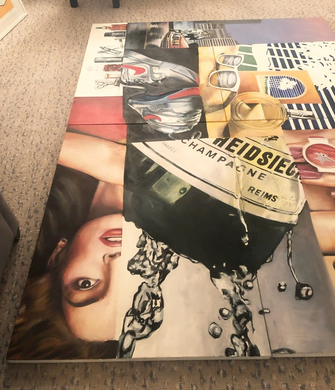 Large pop art painting laid on the floor, depicting a collage of champagne bottles, a woman's face, and various everyday objects like sunglasses and a soda can. The vibrant, detailed composition blends realism and abstract elements, creating a dynami