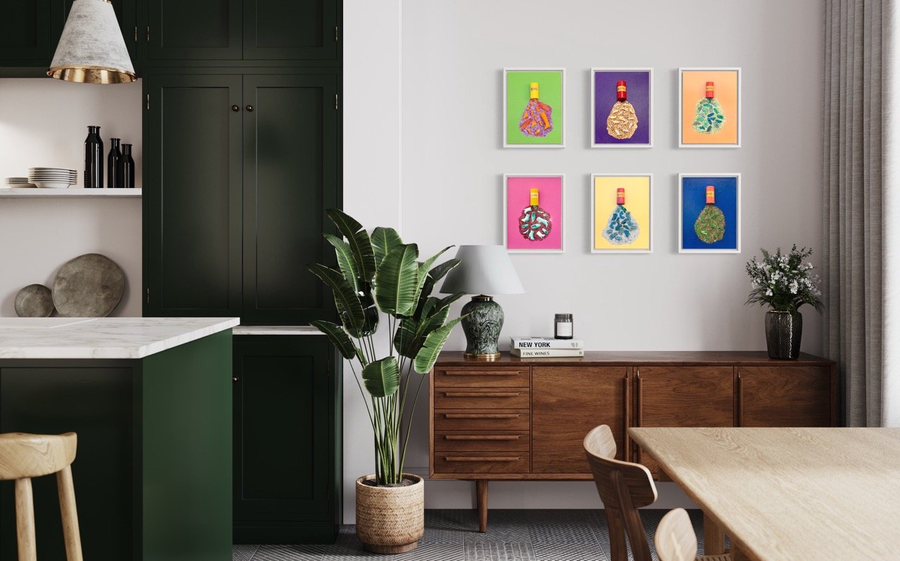 Six colorful canvases with pill bottles spilling out barbie shoes and glitter hanging in a green kitchen above a wooden console.