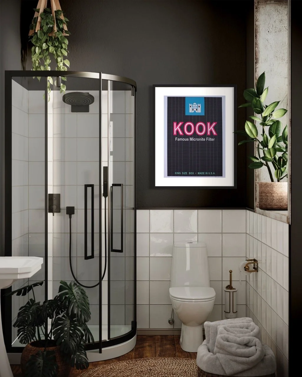 Modern bathroom featuring a glass-enclosed shower, white tiled walls, and a framed "KOOK" artwork with pink lettering on a black background. The space includes a white toilet, potted plants, and rolled towels on the floor.