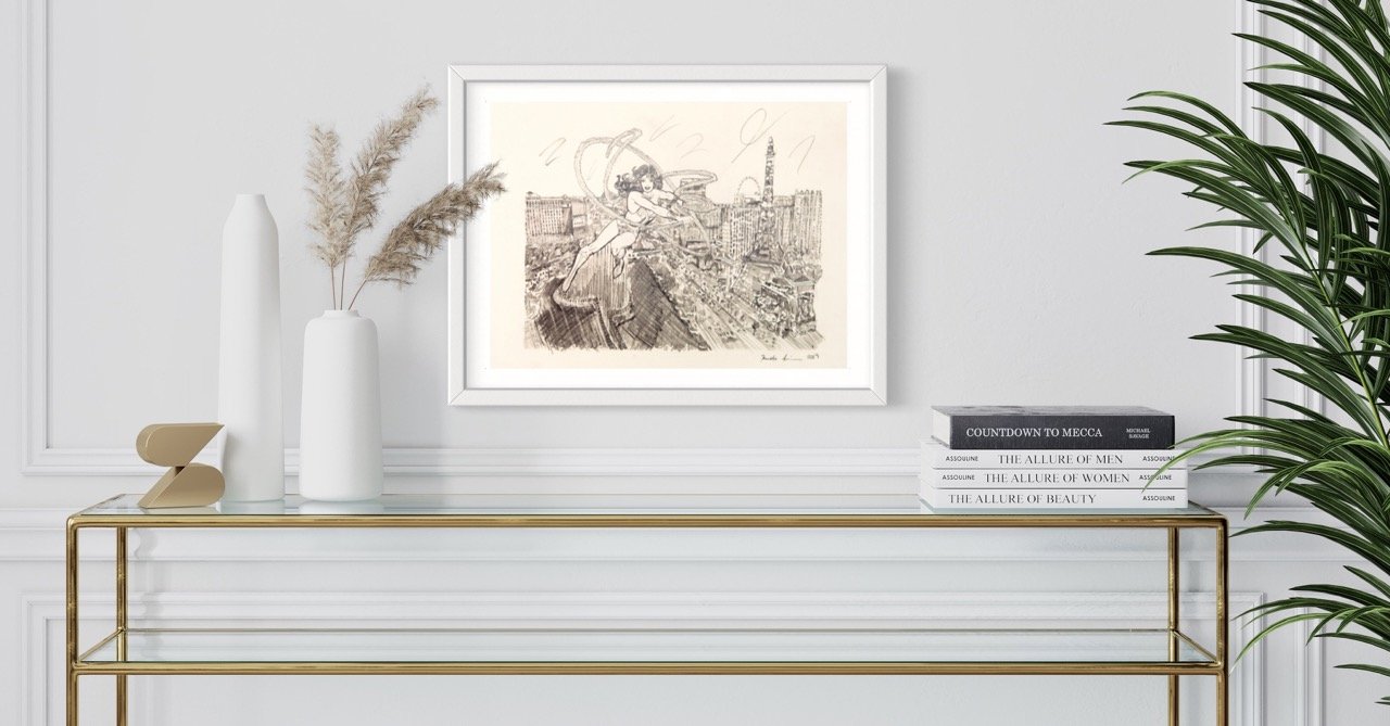 "A framed sketch of wonder woman flying over Las Vegas, hanging on a wall complemented by a modern vase with pampas grass and a stack of fashion books on a gold console table."