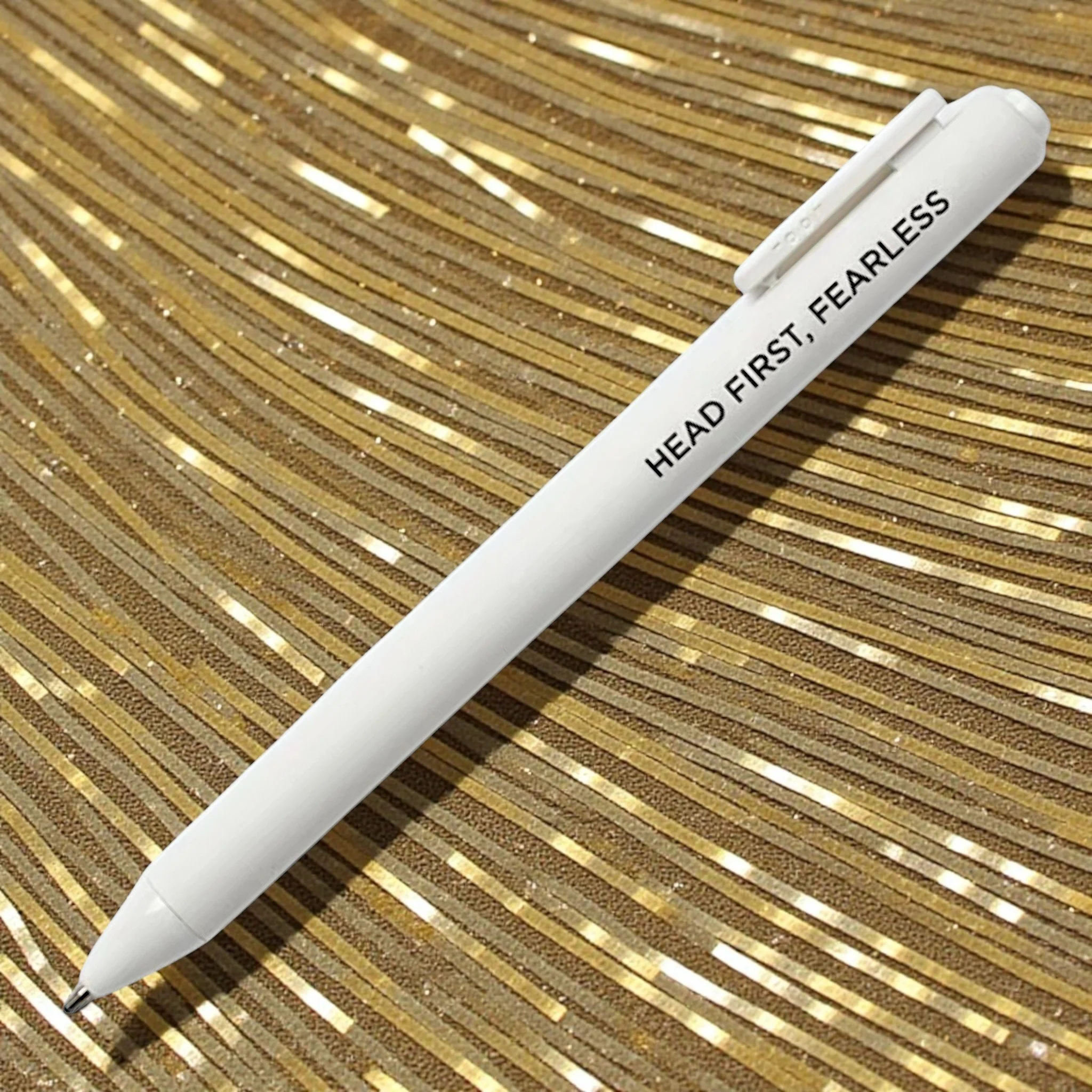 Taylor Swift lyric-inspired white pen with the phrase “HEAD FIRST, FEARLESS” on a sparkly gold background.
