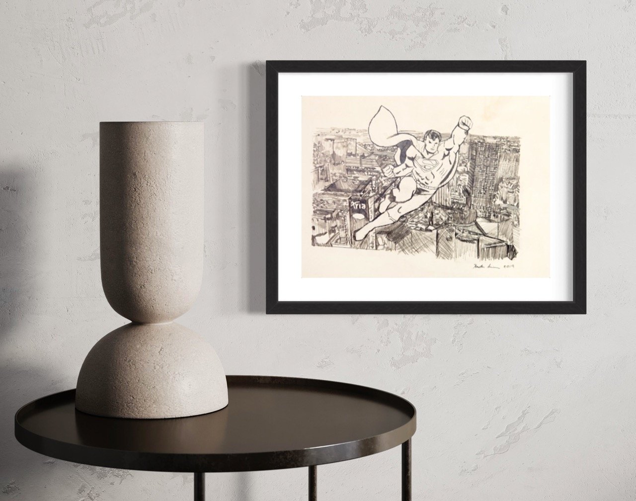 "Framed monochrome pencil illustration of a superman flying over a detailed cityscape, displayed on a textured wall beside a unique two-tiered stone vase on a circular table."