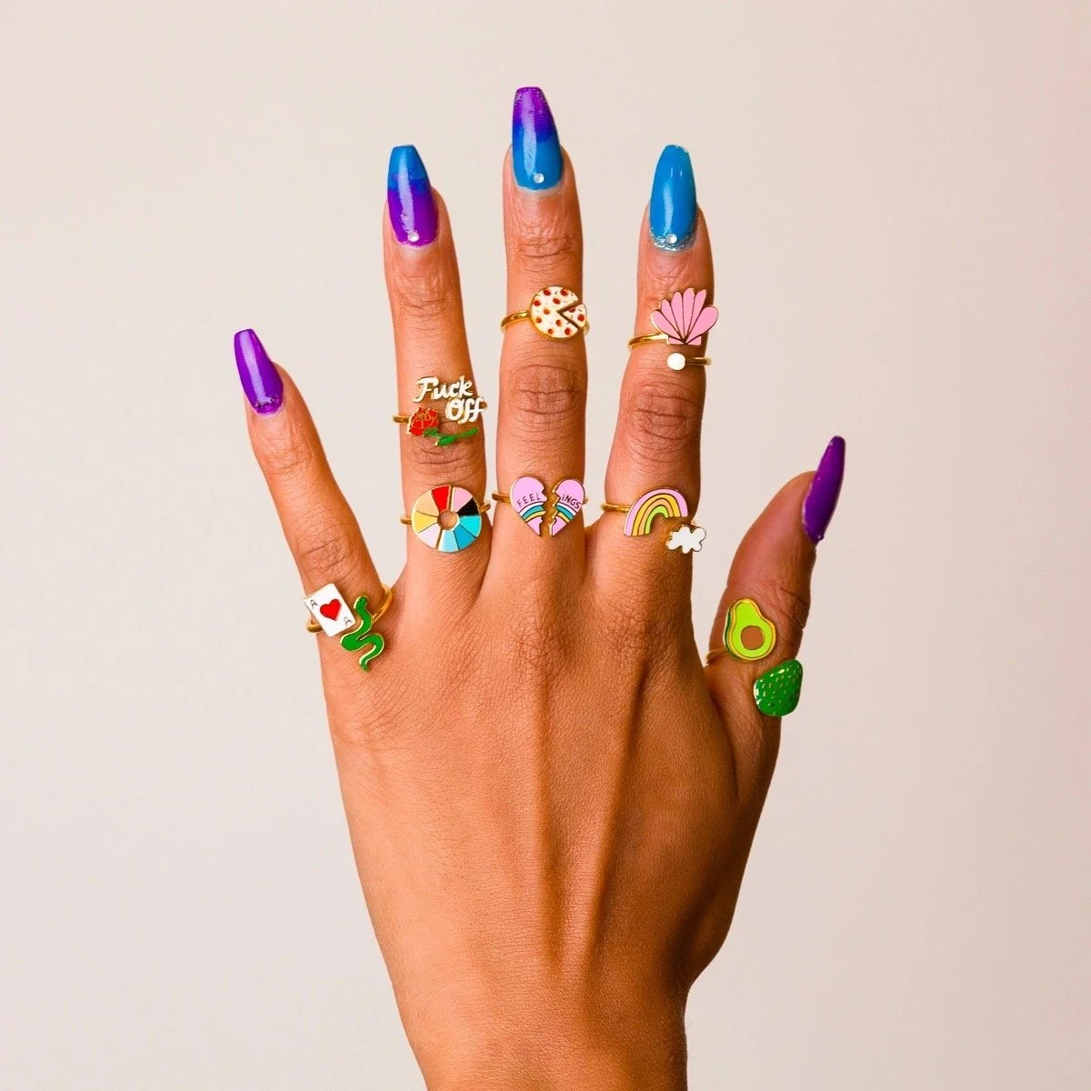 Hand wearing a colorful stack of adjustable enamel rings with playful art, food, rainbow and novelty designs