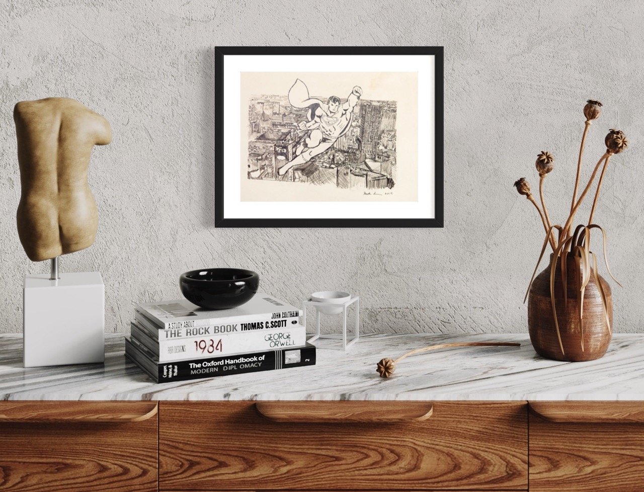 A framed sepia sketch of superman soaring above city skyscrapers by artist Kristin Simmons on a textured wall, complemented by an abstract sculpture and a rustic vase with dried flowers on a marble countertop.