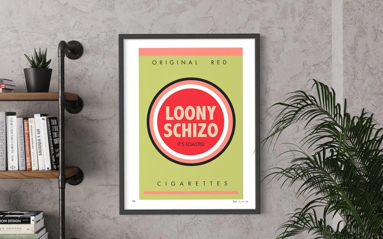 Framed pop art poster with a retro cigarette pack design, labeled "LOONY SCHIZO" in bold red and white. Text reads "ORIGINAL RED" and "IT'S TOASTED." The background is green with a red border. The poster is displayed on a concrete wall beside a books