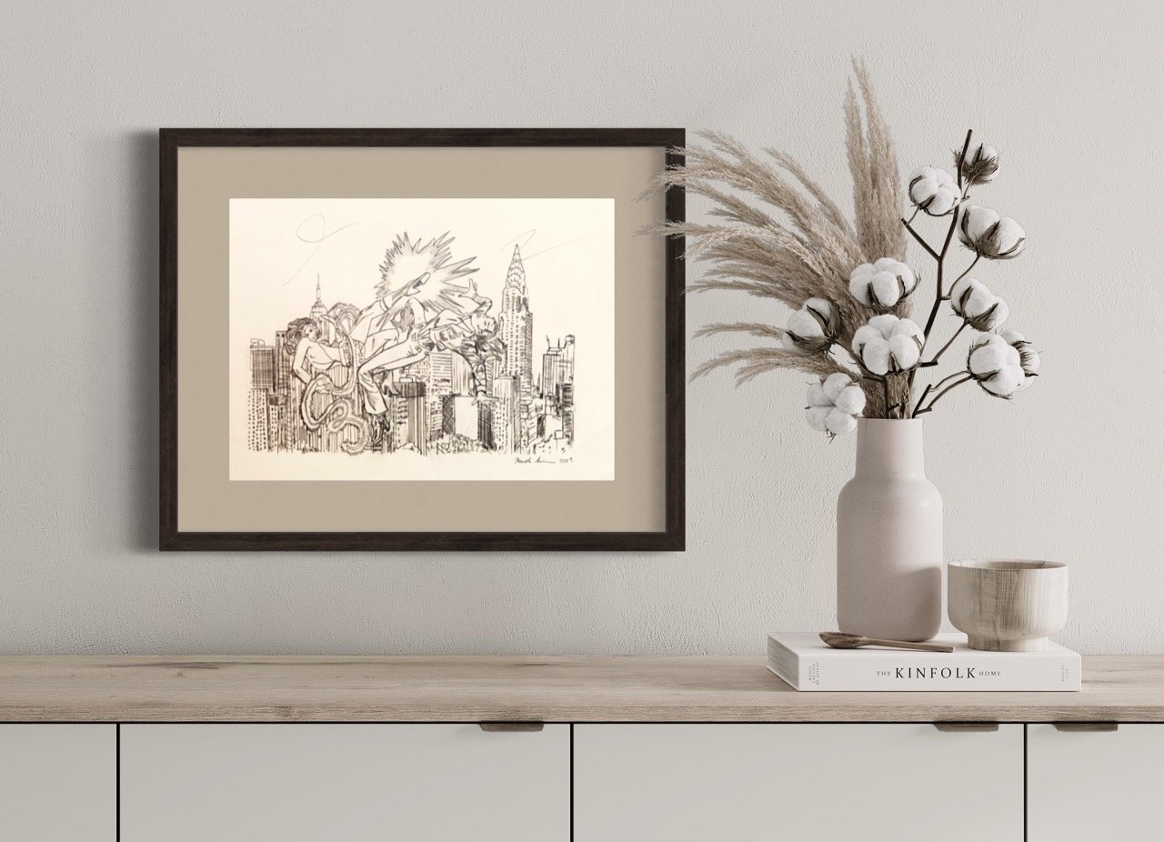 Framed pencil drawing of an animated cityscape with Wonder Woman fighting another woman, presented on a wall beside a vase of cotton stems and pampas grass, resting on a shelf with a book and bowl.