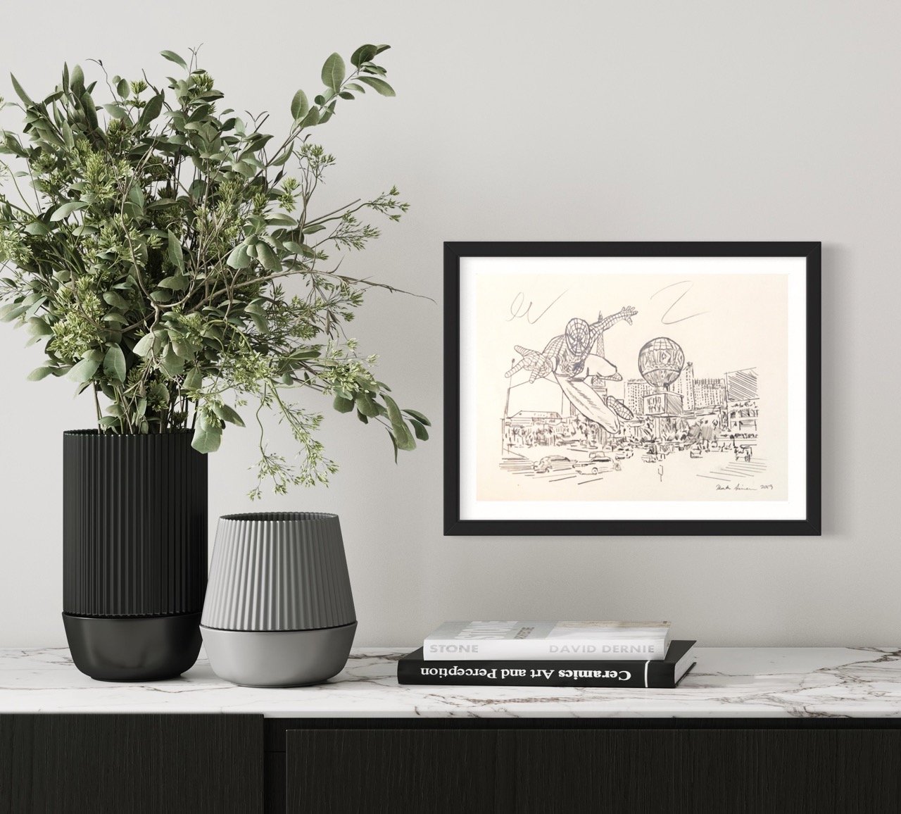 A framed artwork by Kristin Simmons, depicting spiderman in mid-flight over a bustling cityscape, prominently displayed on a light-colored wall above a dark, wood-grain credenza.