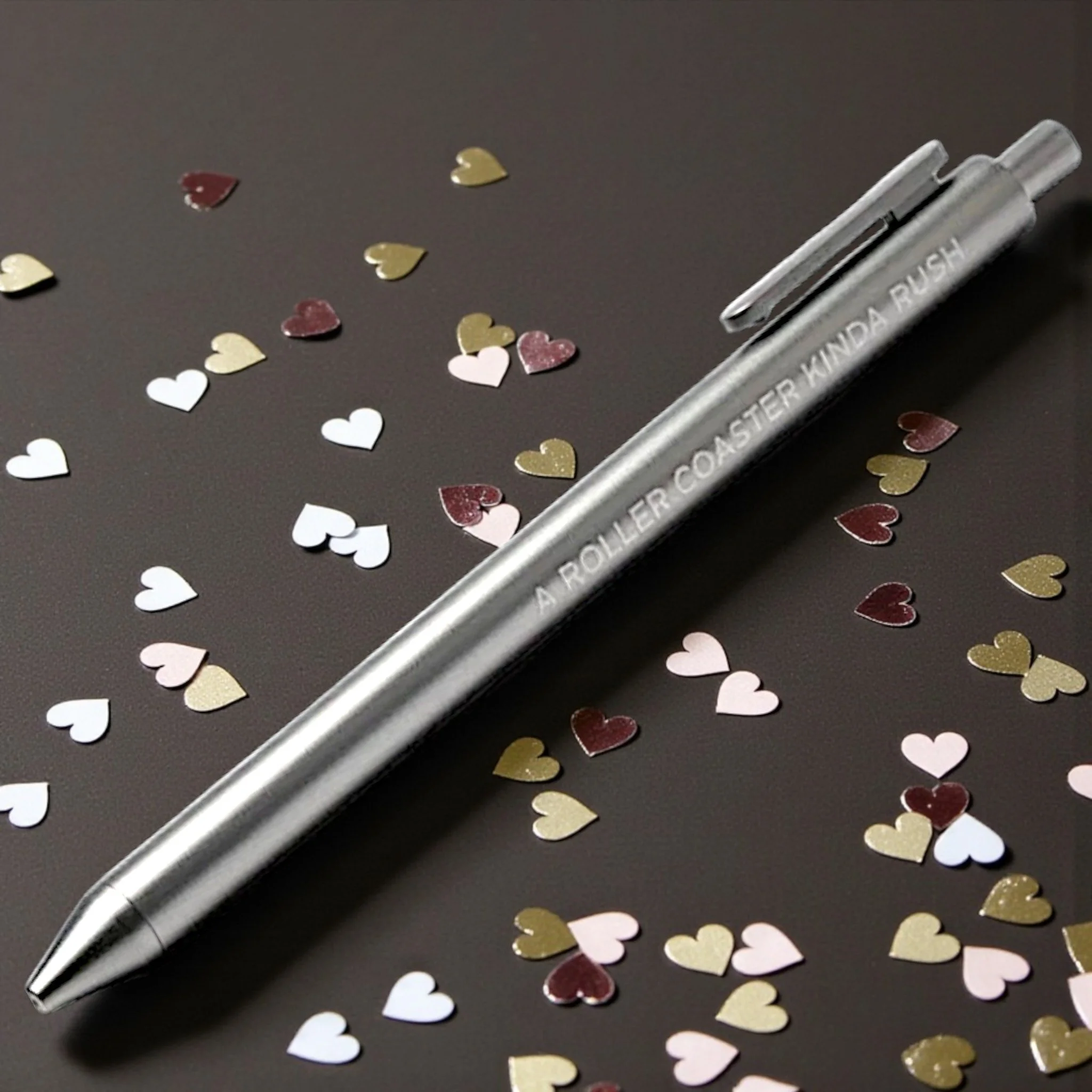 Silver Taylor Swift-inspired pen engraved with “A ROLLER COASTER KINDA RUSH,” styled with heart confetti for Swiftie vibes.