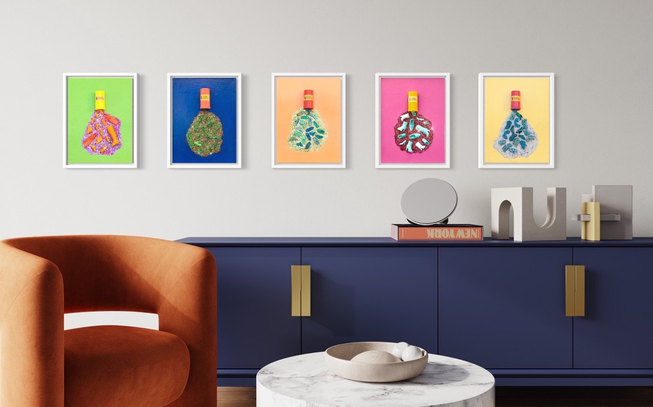Five vertical pop art canvases with pill bottles spilling out barbie shoes hanging above a blue cabinet.