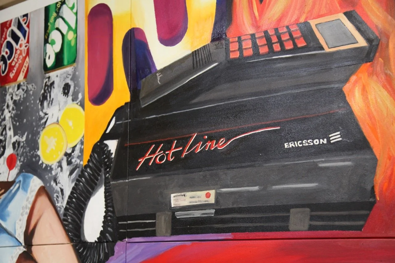 Bold pop art piece showcasing an Ericsson Hotline phone with a black curly cord. The background is decorated with colorful images of citrus slices and soda cans, merging retro technology with vibrant modern art.