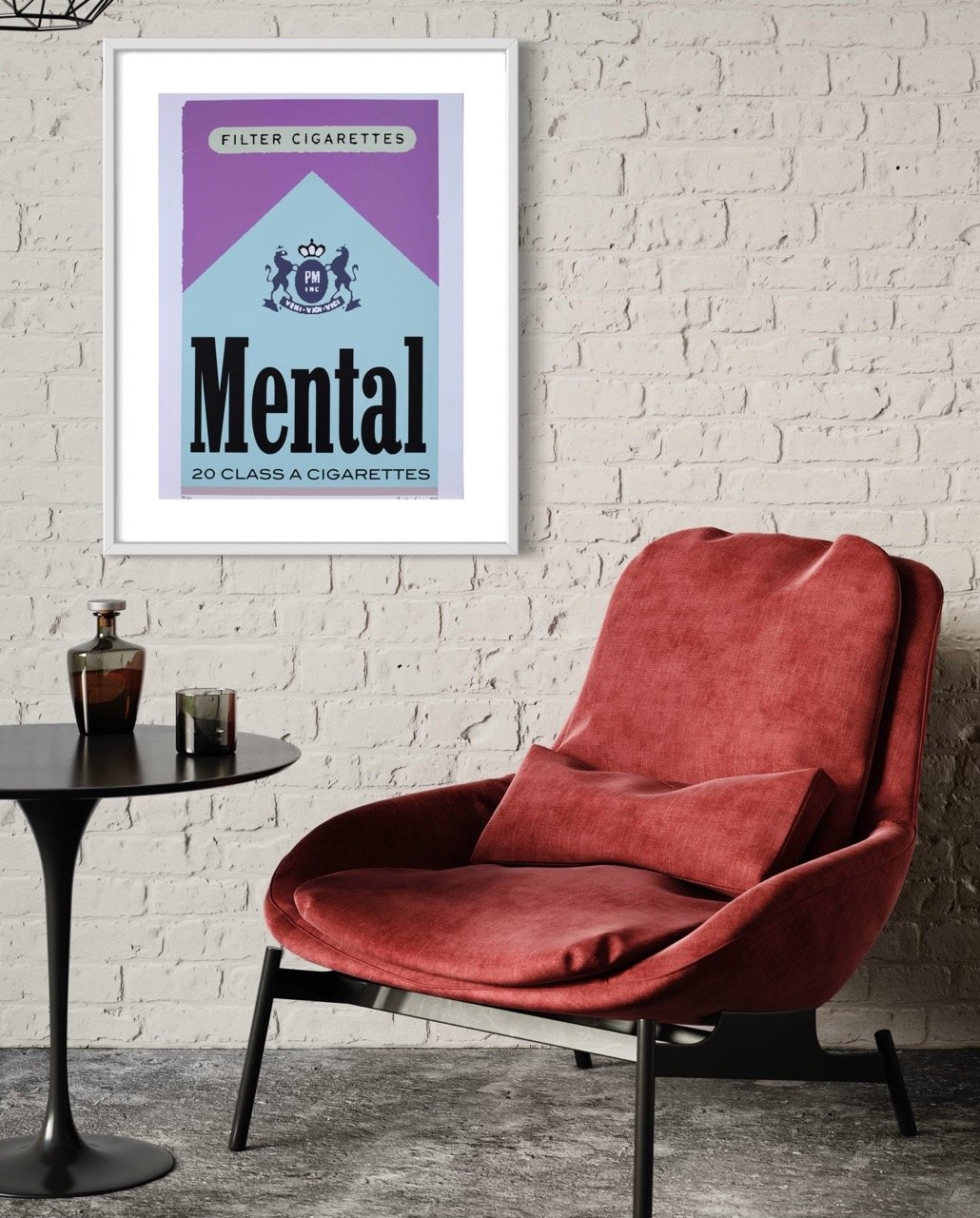 Silkscreen artwork prominently displaying the word 'Mental' in bold lettering with various designs and colors in the background. The framed piece is mounted on a white brick wall adjacent to a plush red chair and a side table with a beverage glass.