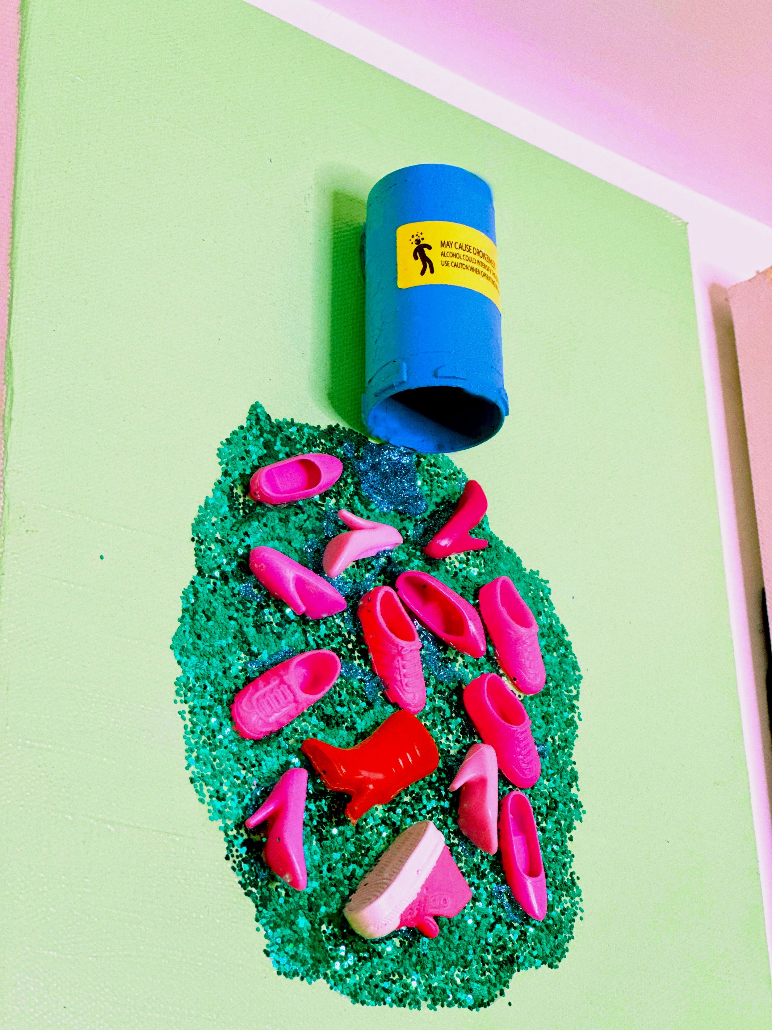 Mixed media art piece featuring a blue pill bottle spilling out pink toy shoes onto green glitter on a light green canvas.