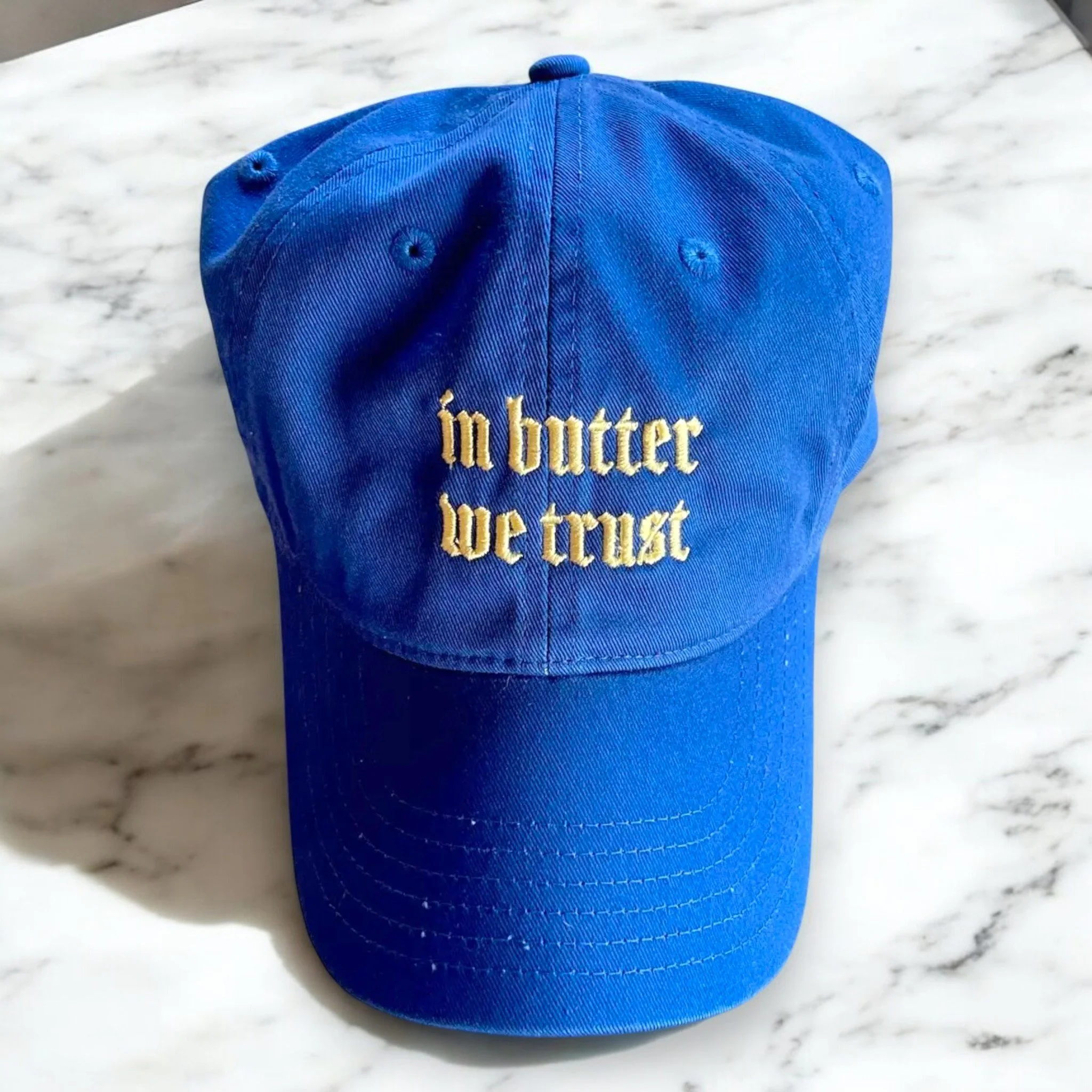 “In Butter We Trust” embroidered hat in bold blue, perfect for fans of funny food fashion.