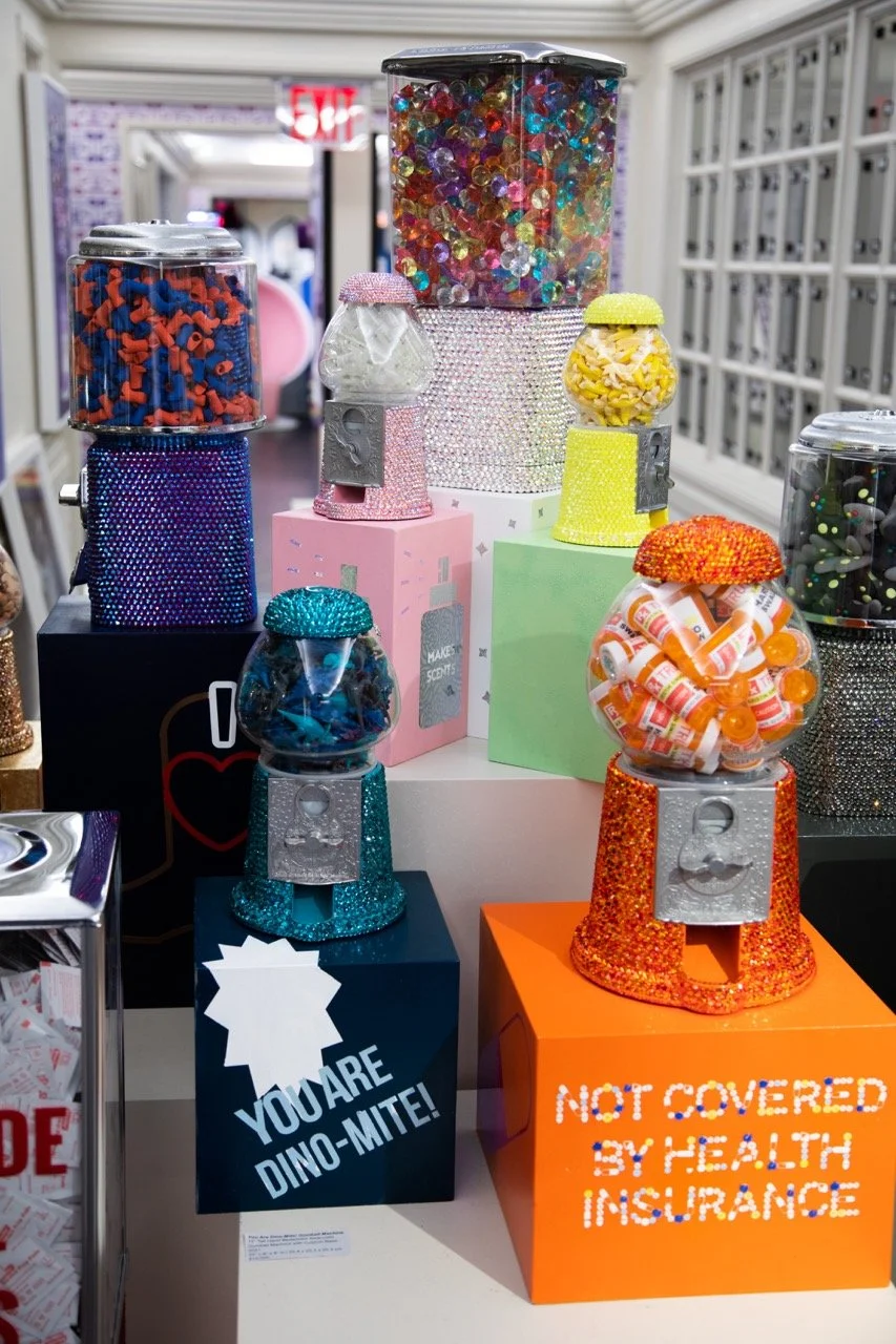 A selection of Kristin Simmons' 'Glamour Gumballs' sculptures at Bergdorf Goodman, with messages like 'YOU ARE DINO-MITE!' and 'NOT COVERED BY HEALTH INSURANCE'.