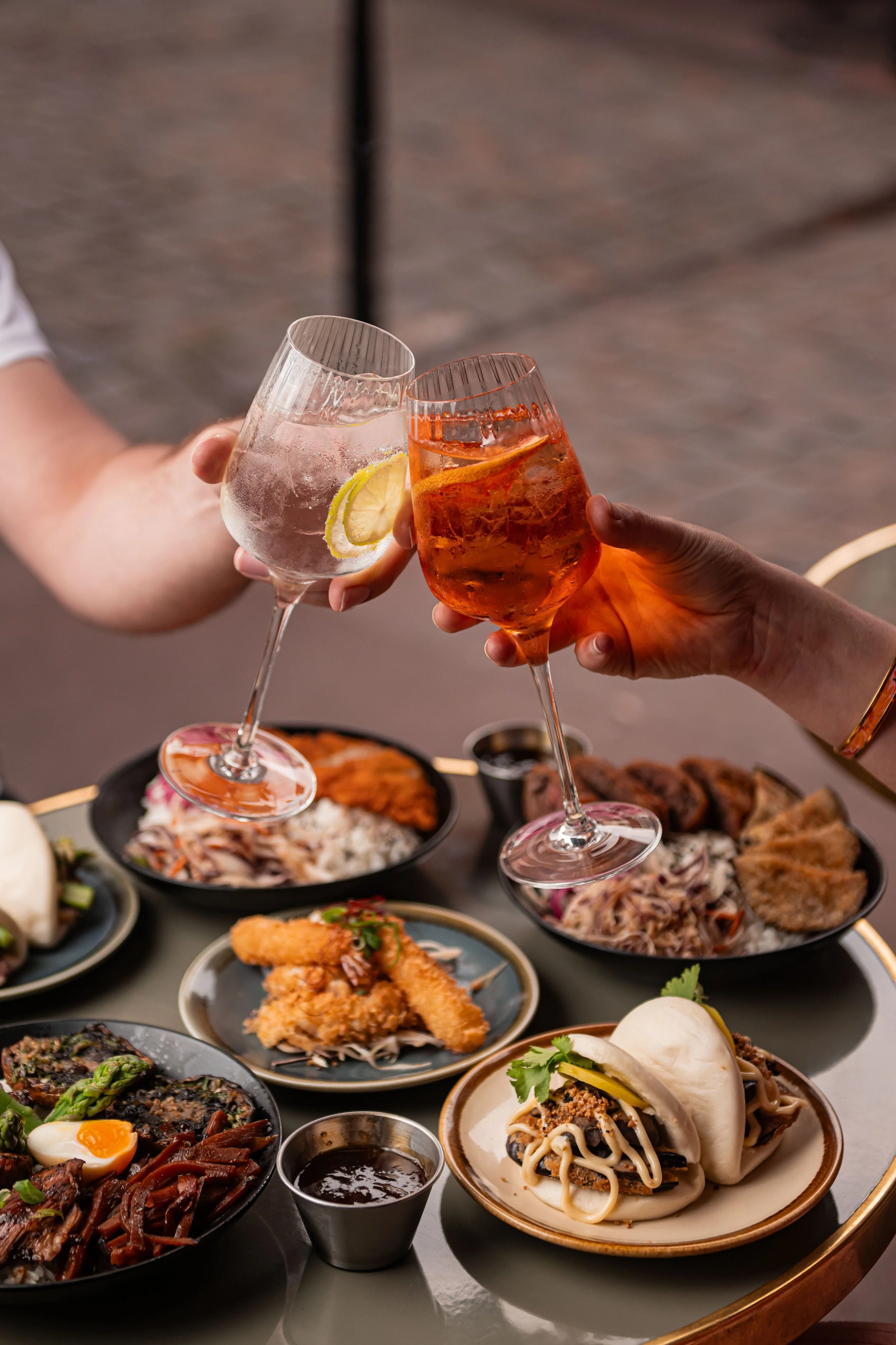 Célébration avec deux personnes toastant avec deux verres de cocktails, entourées de divers plats japonais comme ramens, sushis, tempuras, et autres mets traditionnels.