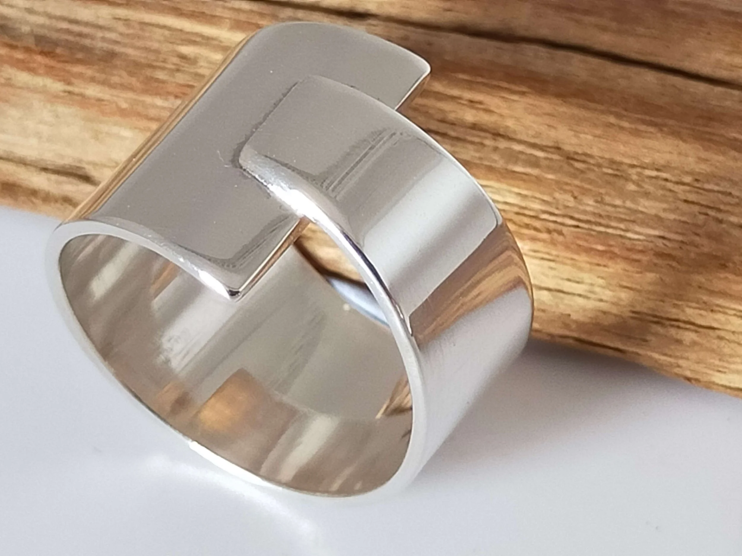 Close-up of a silver open cuff bracelet on a wooden surface.