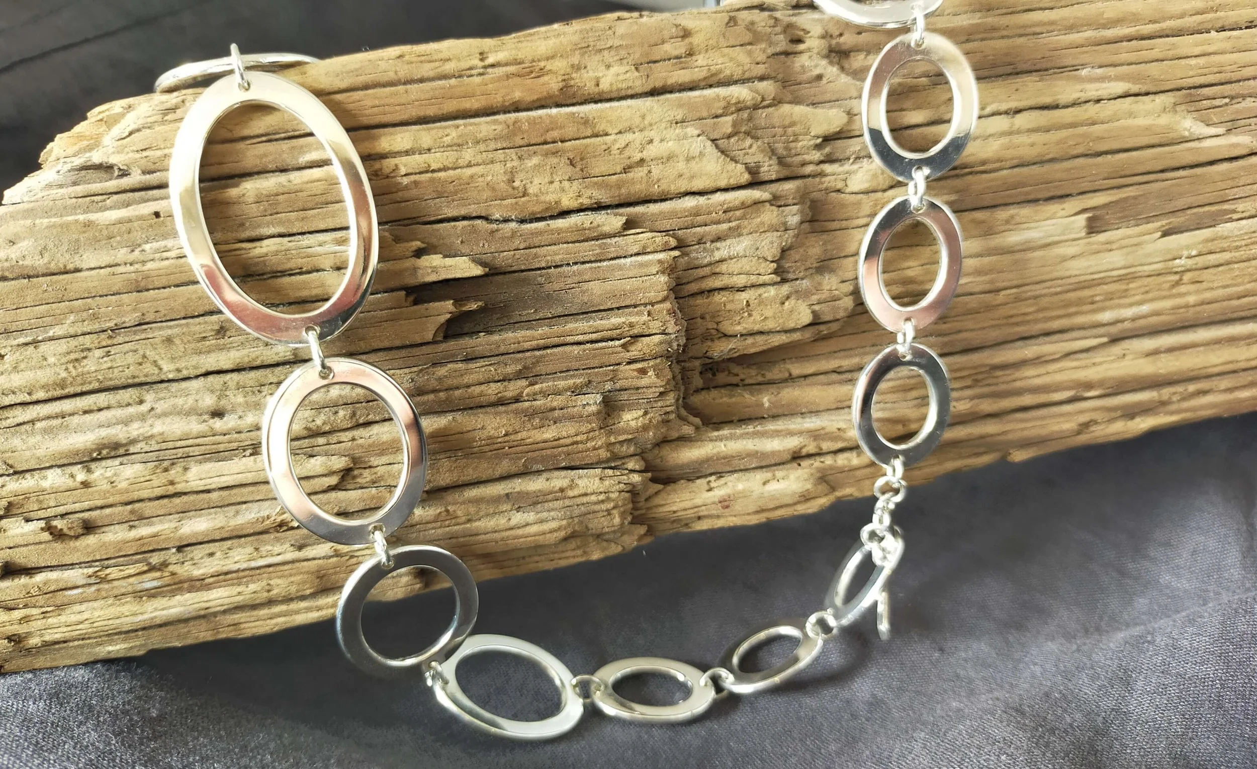 Silver oval link necklace on a rustic wooden stand.