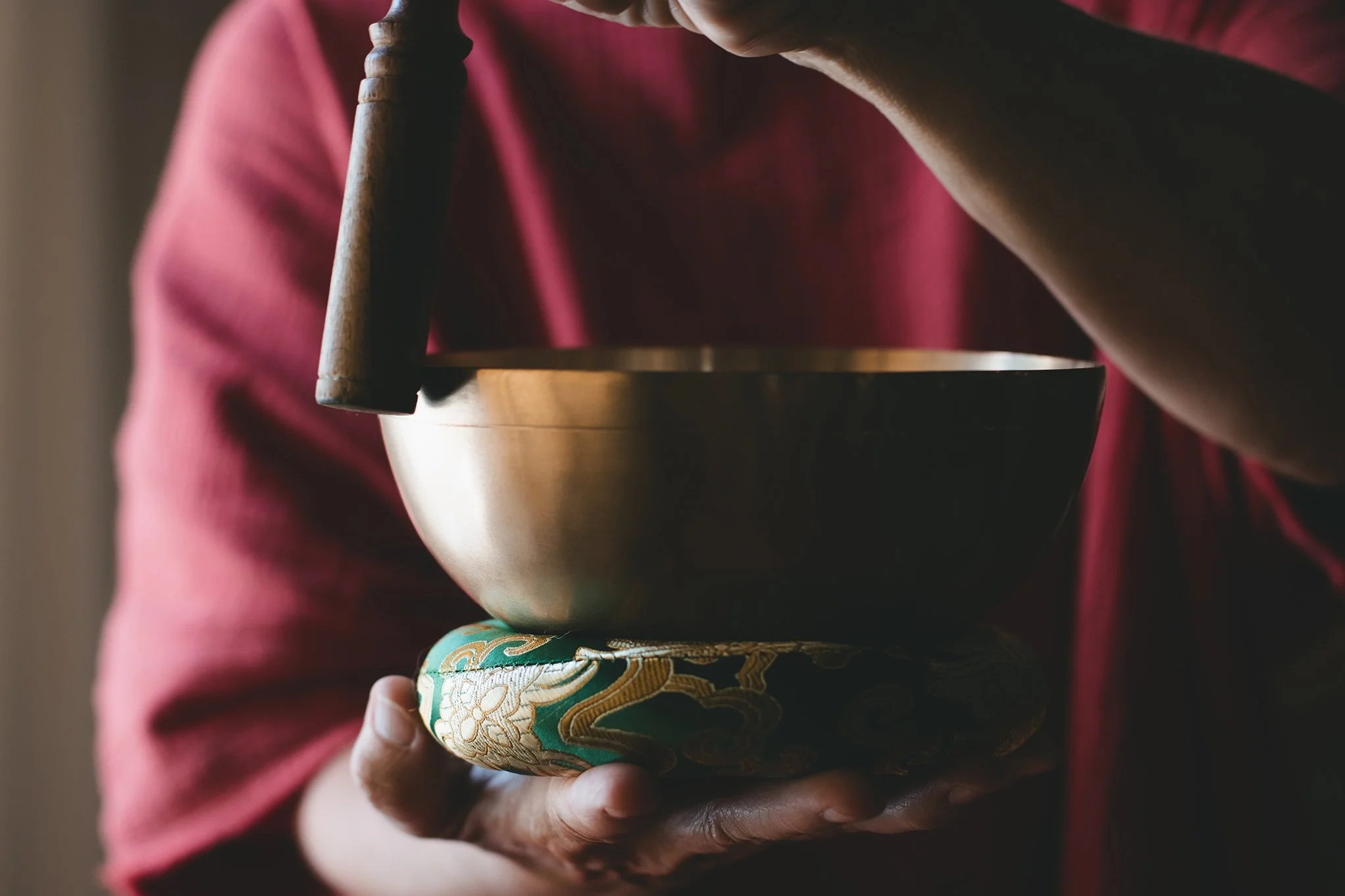 Person holding a metallic singing bowl on a decorated cushion.