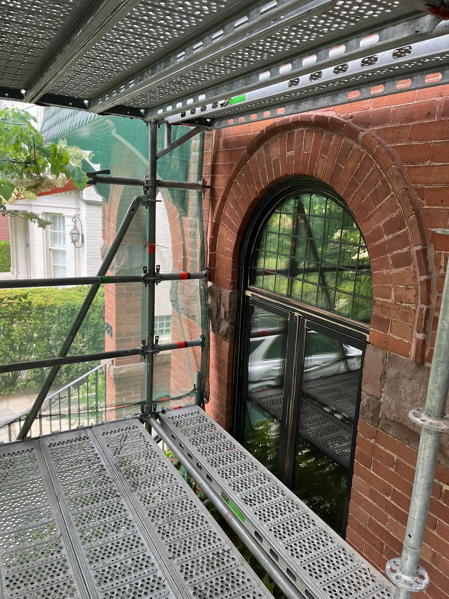 Scaffold with green dust netting for masonry restoration access with arch window on Toronto brick heritage house