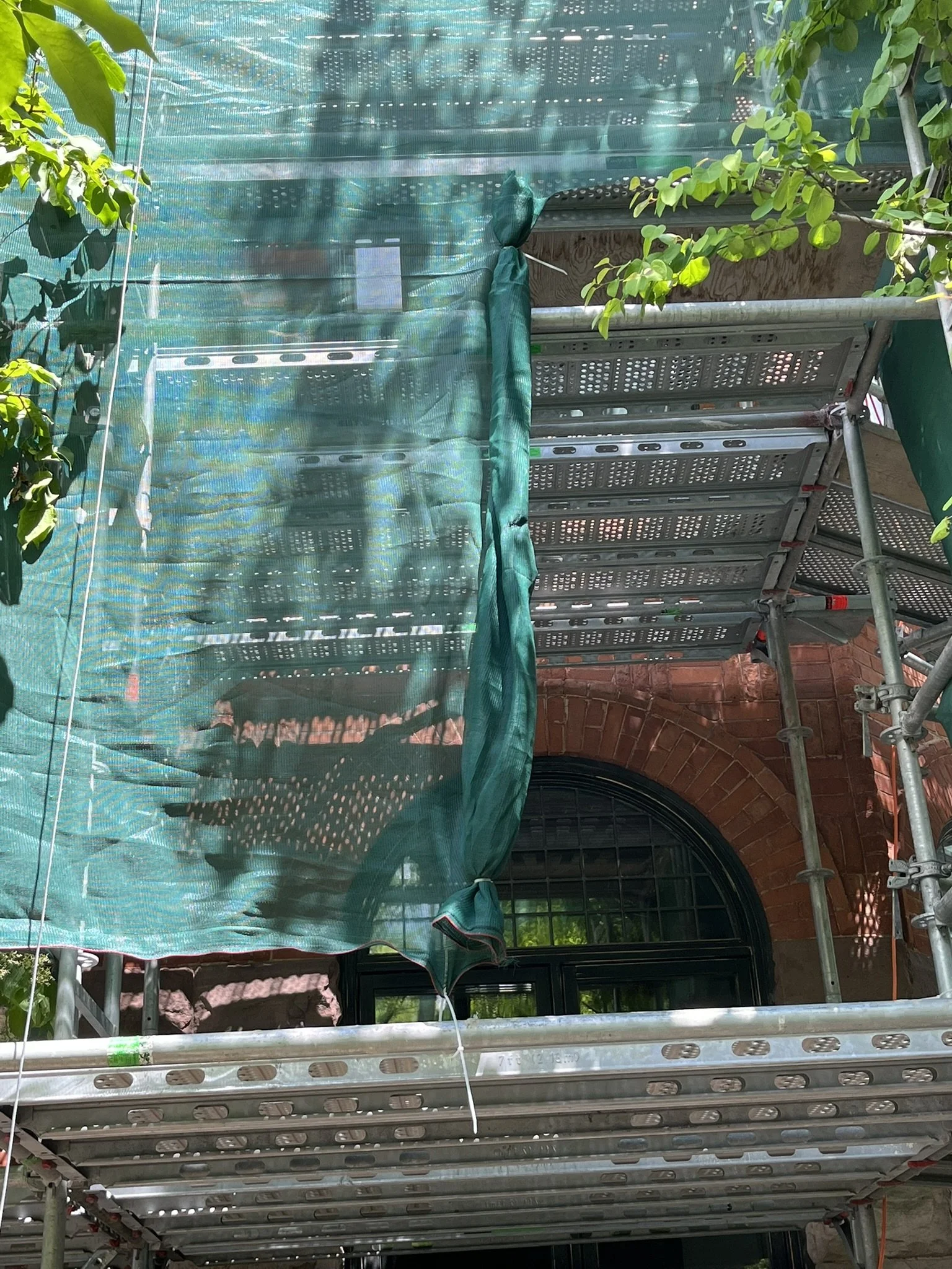Green dust protection netting on a front access scaffold for brickwork restoration