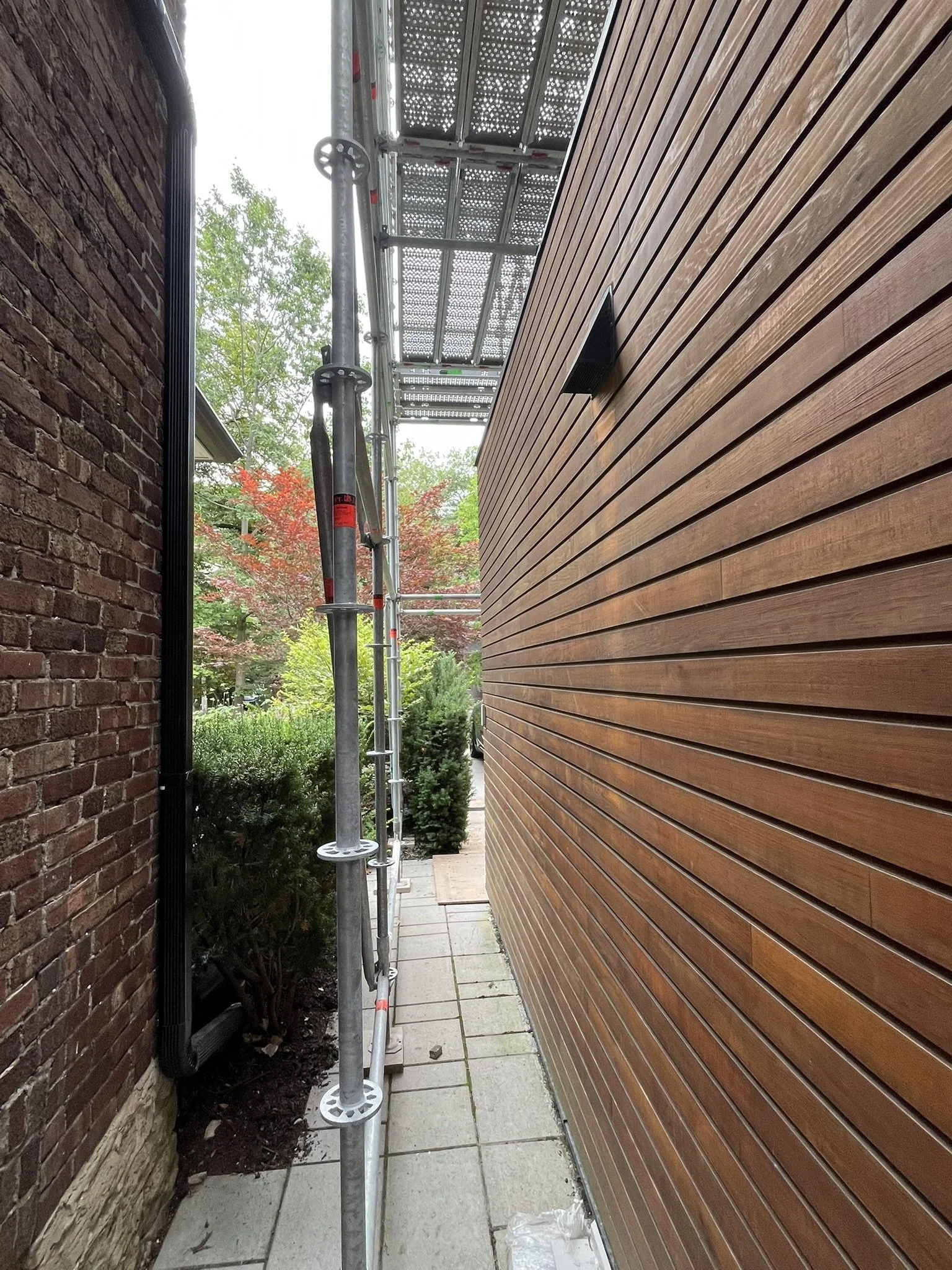 Narrow scaffolding set up between two houses for construction, one wood sided and one brick