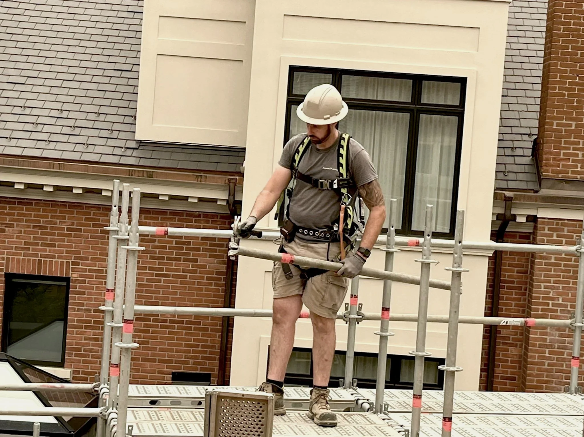 Scaffolder in a hard hat and harness installing scaffold deck