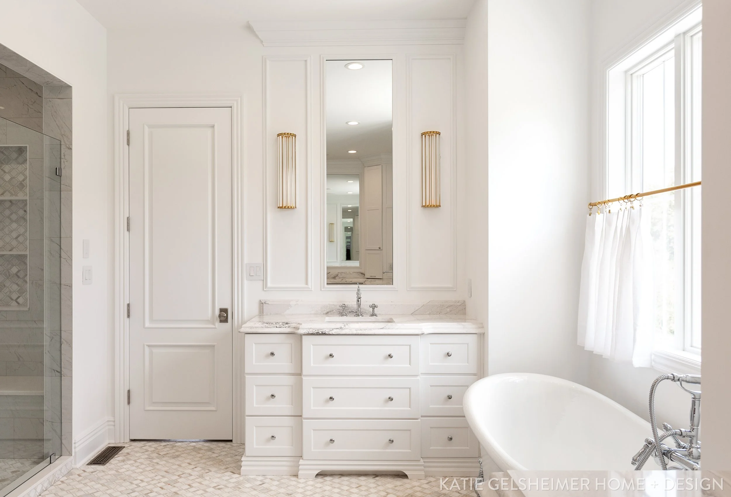 A luxurious white bathroom with a marble countertop vanity, a full-length mirror, gold wall-mounted light fixtures, large window with sheer curtains, a bathtub with a vintage-style faucet, and a marble shower enclosure. custom cabinets, Missouri 