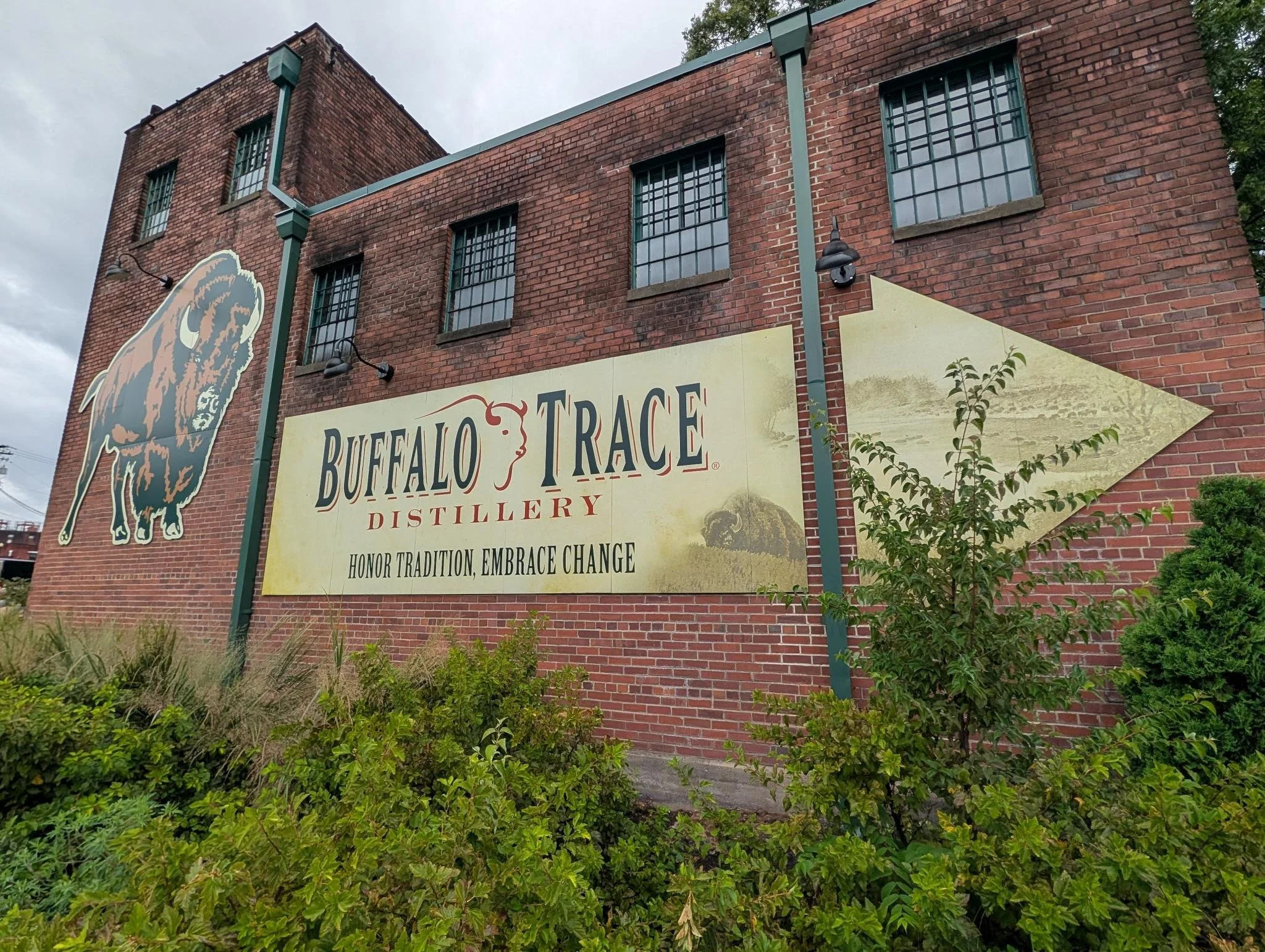 Red brick building with signs for Buffalo Trace Distillery, featuring a buffalo illustration and tagline 'Honor Tradition, Embrace Change'.