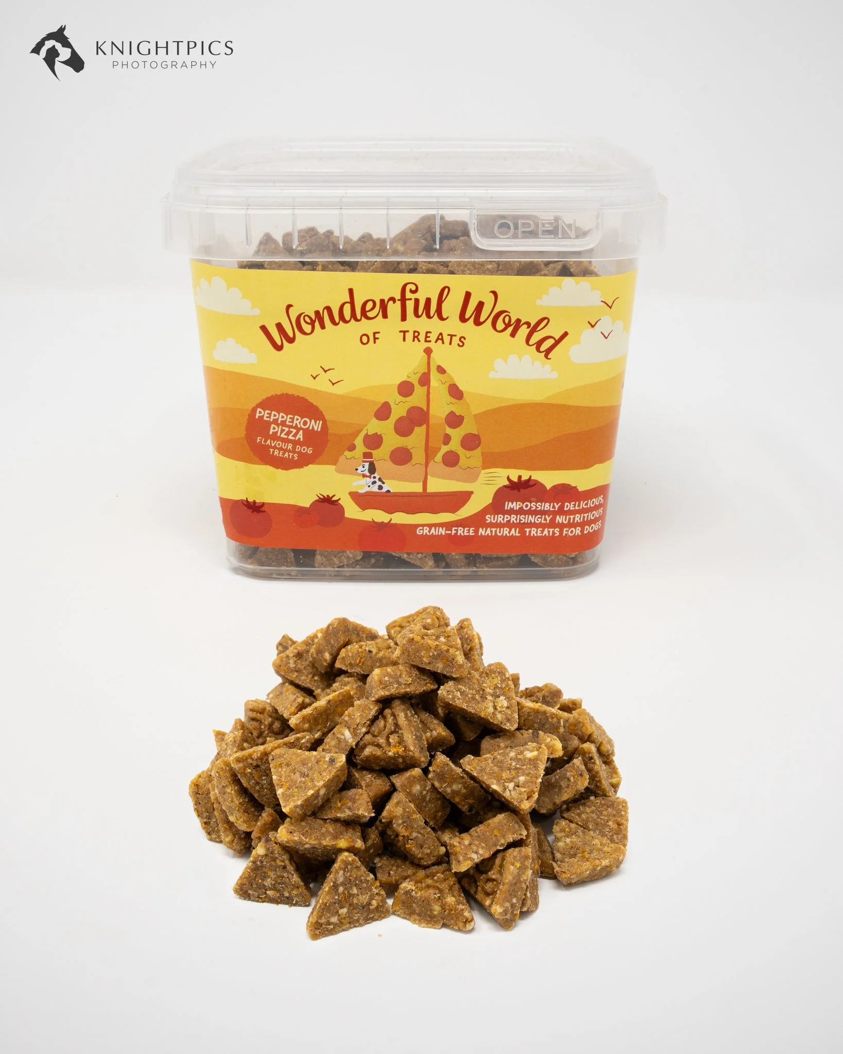 Commercial pet food product photography showcasing a yellow tub of pepperoni pizza flavoured dog treats from The Wonderful World of Treats, with individual triangular treats arranged in the foreground. Captured against a white studio background to cl