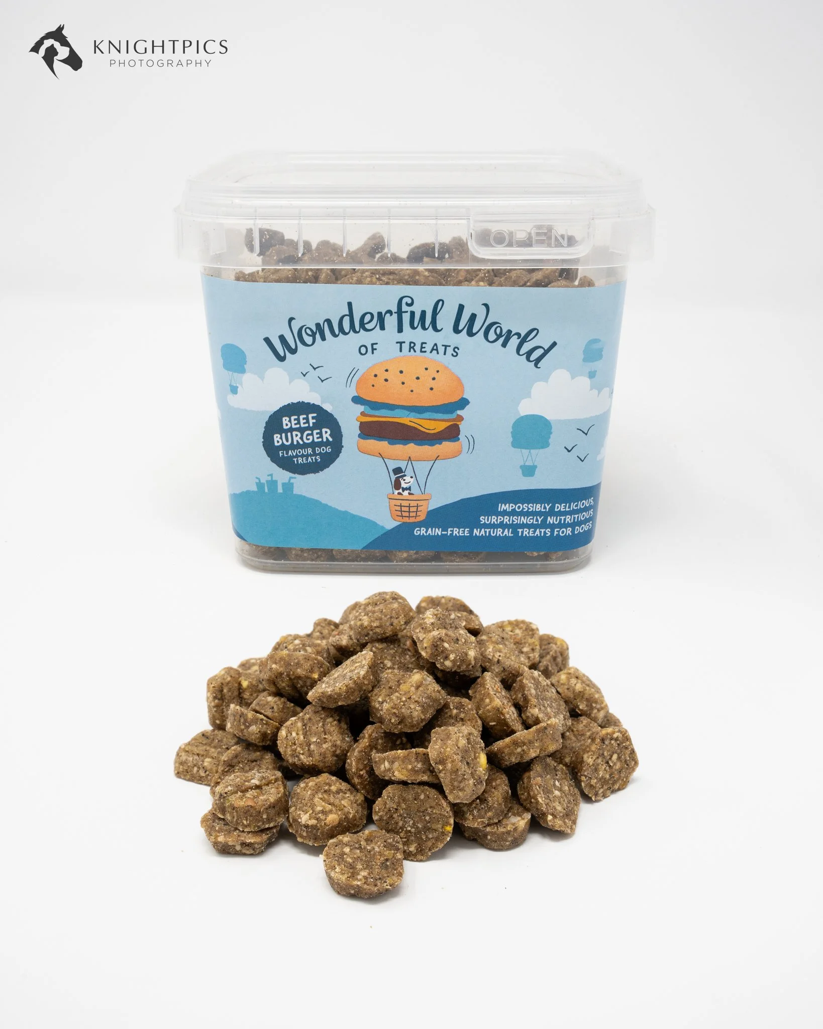 Commercial studio product photography for The Wonderful World of Treats, featuring a blue tub of beef burger flavour dog treats with individual treats arranged in the foreground. Photographed against a clean white background to highlight the packagin