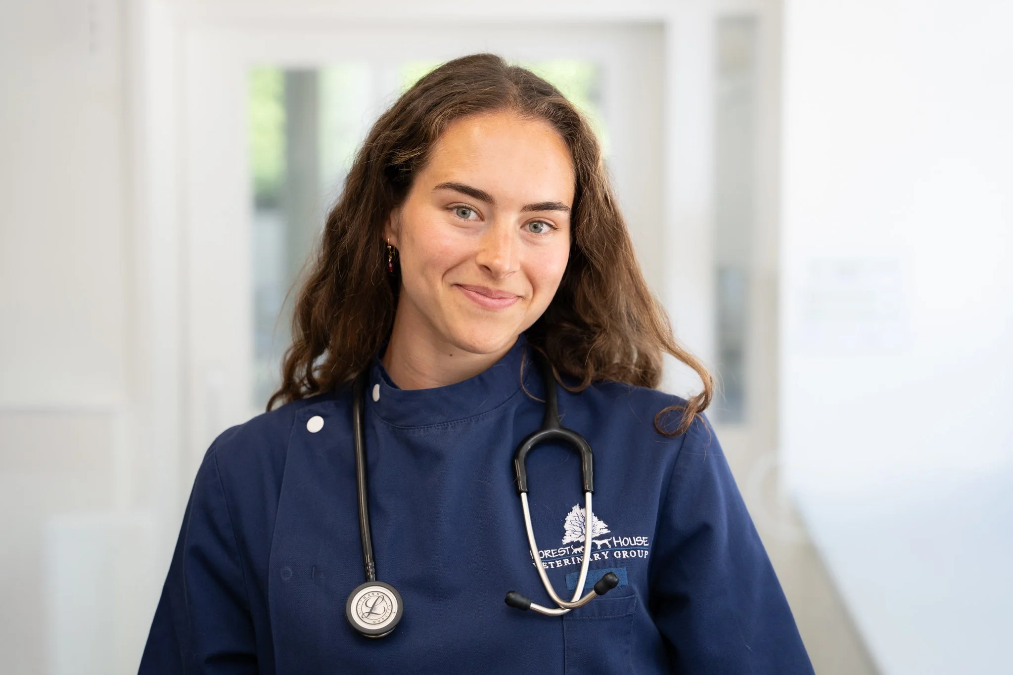 Professional headshot of a smiling female veterinary professional wearing navy scrubs and a stethoscope at Forest House Vets in Windsor. Created for a commercial veterinary branding photography project, this natural portrait presents an approachable 