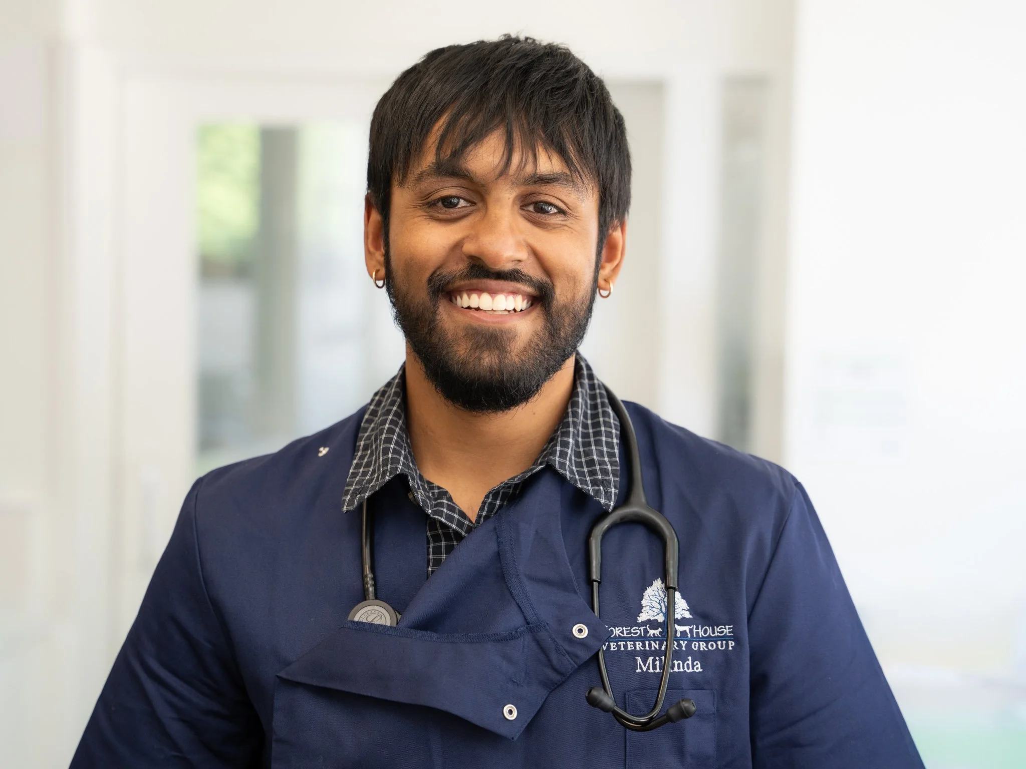 Professional environmental headshot of a smiling male veterinary surgeon wearing navy scrubs and a stethoscope at Forest House Vets in Windsor. Created as part of a commercial veterinary branding photography project, this portrait provides friendly, 