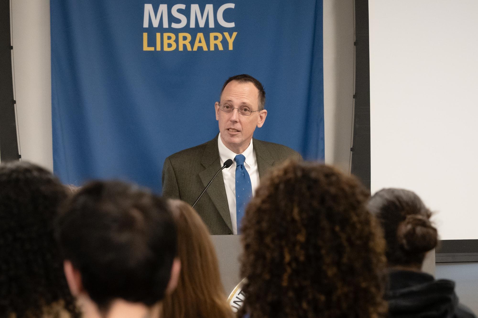 Photo of a speaker at a podium with "MSMC Library" above their head.