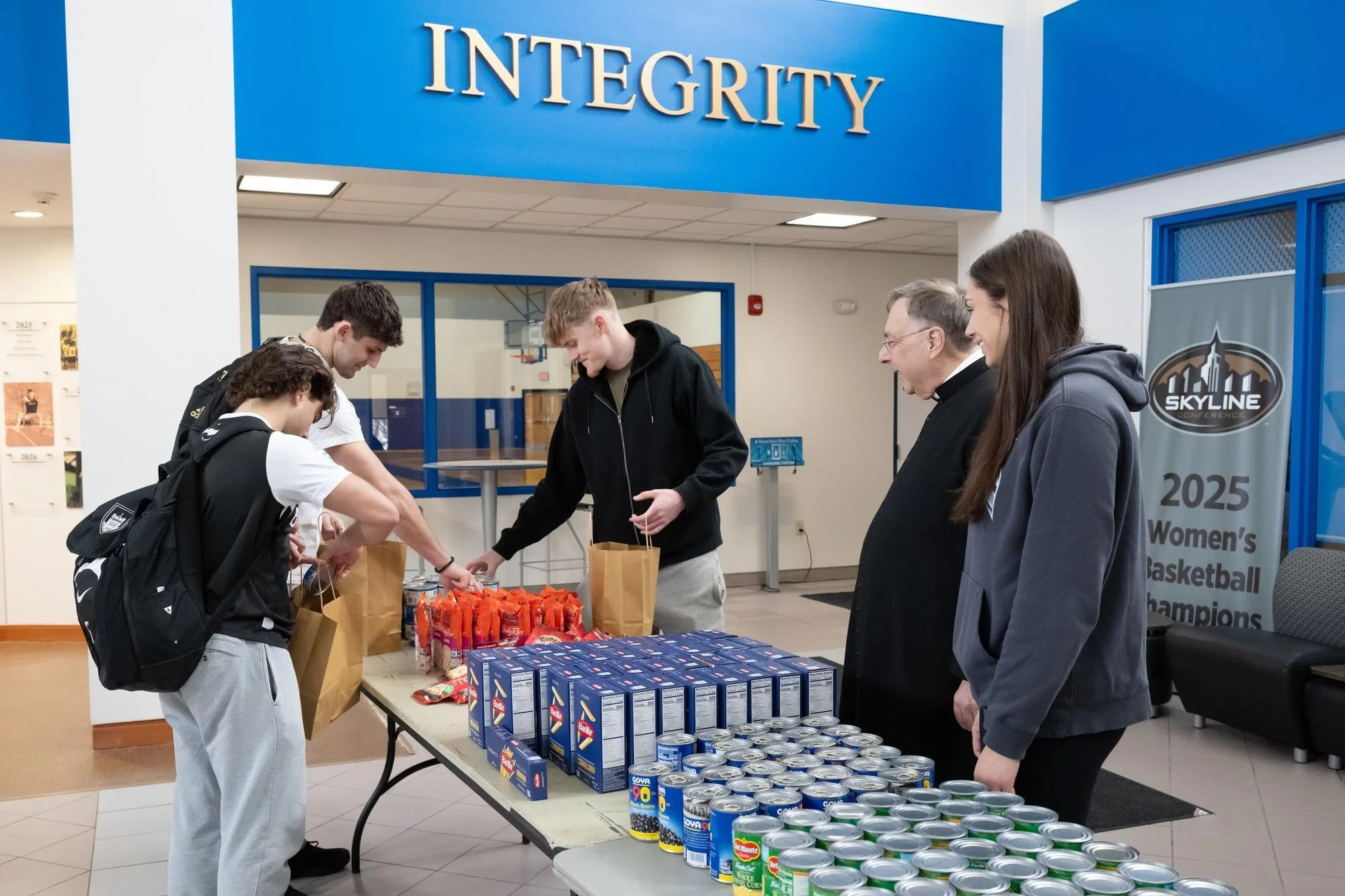 Student athletes pack bags using the donated food on a table in front of them.