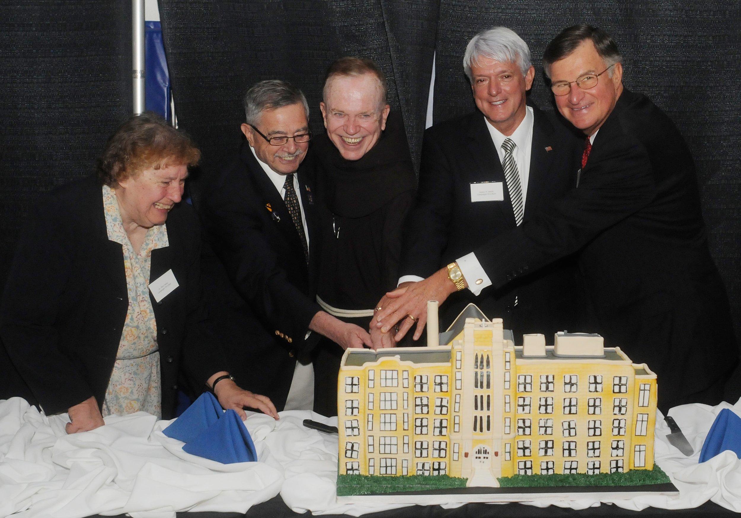 Five members of the college community cut into a cake designed to look like the Dominican Center.